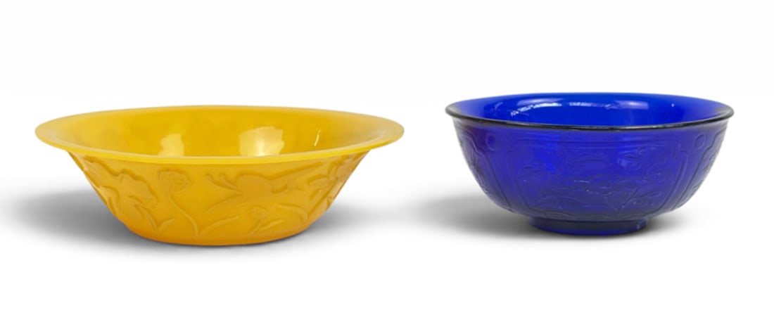 Two 20th Century Chinese Peking Glass Bowls.: The lot contains a cobalt blue bowl and a larger yellow bowl. They both have raised flower decorations on the outside. The smallest bowl measures 2 3/4" tall and 6 1/4" in diameter, and the largest bo