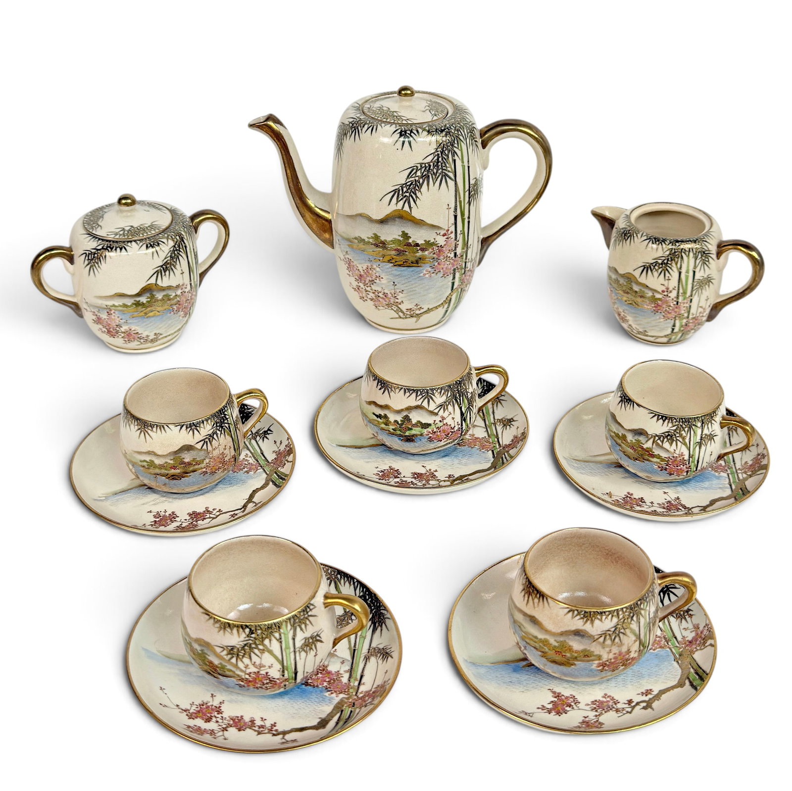 Koshida Kyoto Made Japanese Satsuma Tea Set.: The set has a bamboo pattern, with mountain and water landscapes and flowering trees. It consists of a tea pot, sugar and creamer (the creamer is missing its lid), and 5 cups and saucers. The set look