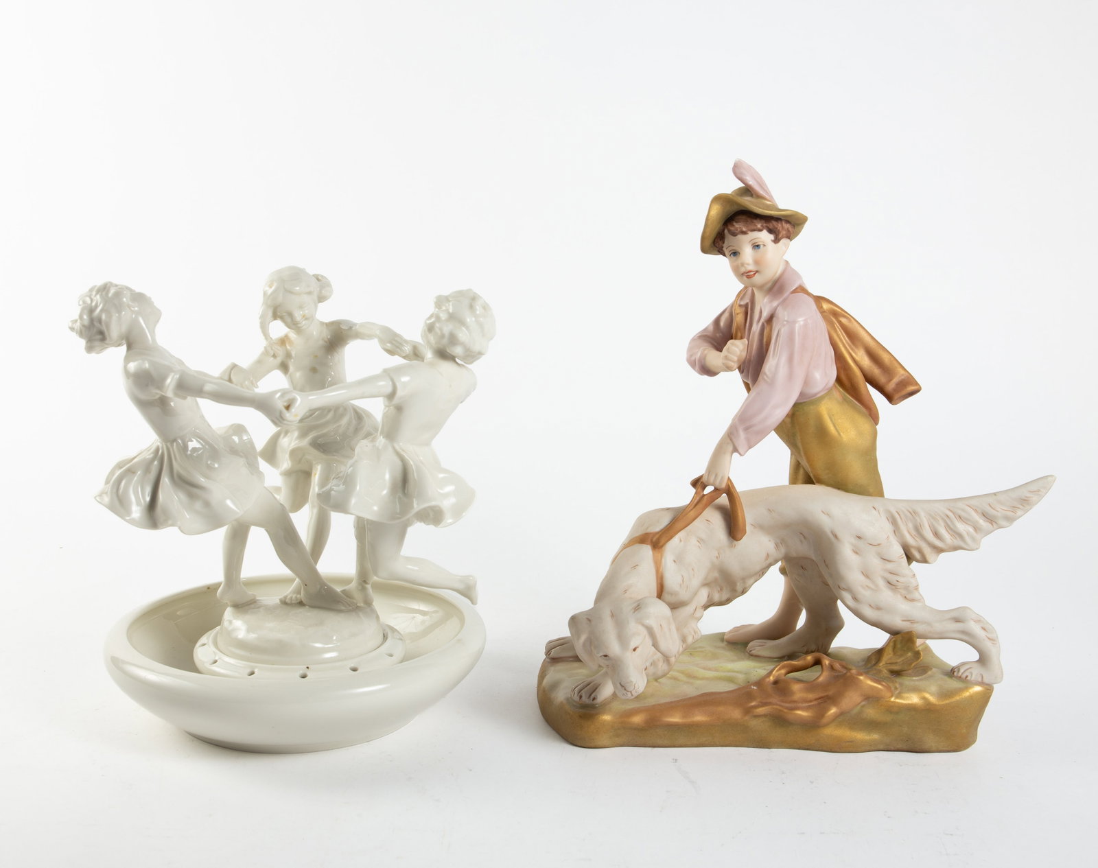 Lot: Hutschenreuther Dancing Girls, Royal Dux Boy.: This lot includes a two-piece Hutschenreuther white flower frog of three little girls holding hands and dancing, and a Royal Dux painted figure of a hunter boy with his pointer dog. The boy has a smal