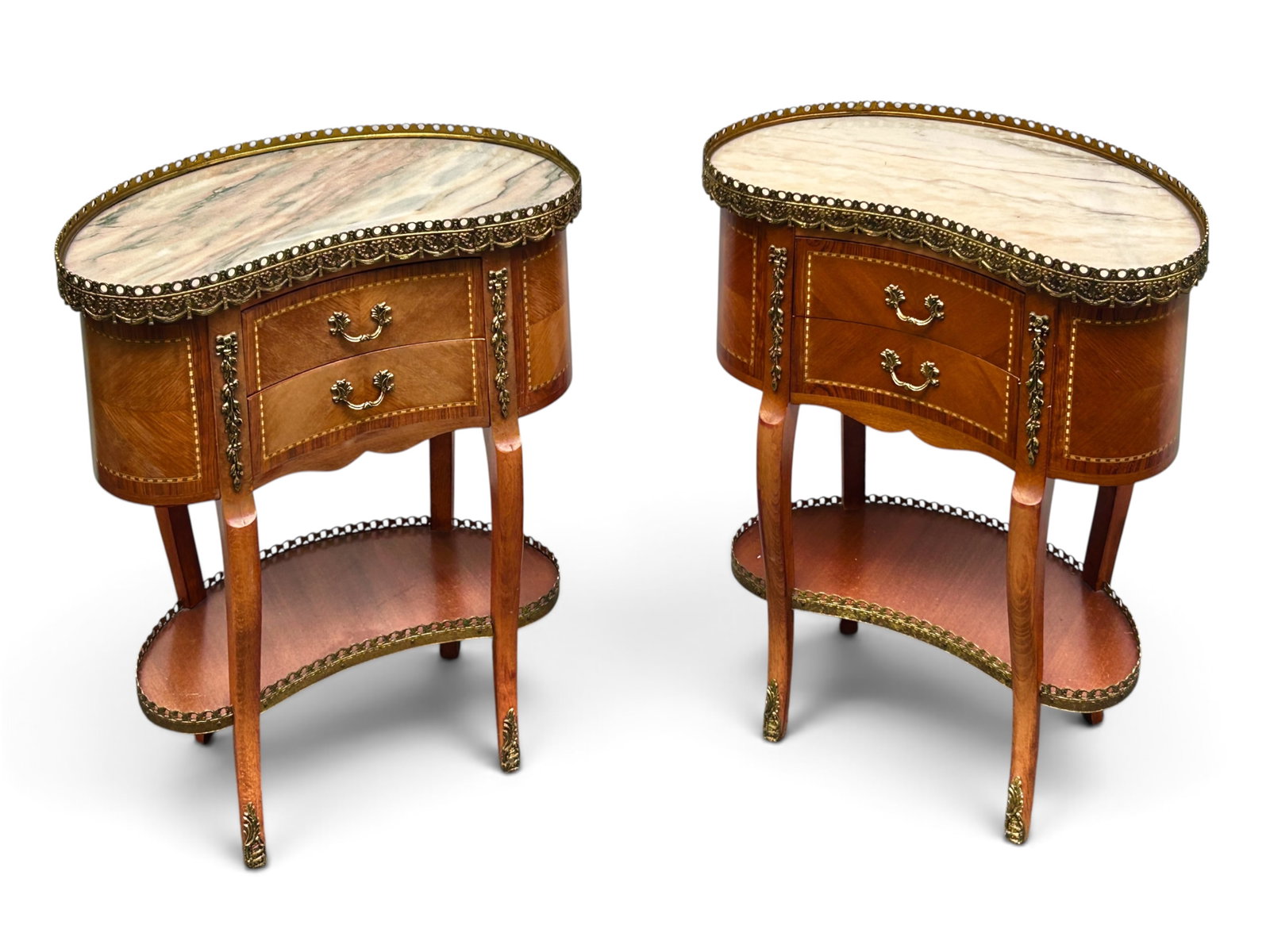 French Kidney Shaped Marble Top Side Tables.: The pair of Louis XV style nightstands or side tables have light-toned marble tops, brass galleries, 2 drawers, and a lower tier with a brass gallery. The drawer section has marquetry designs and orna
