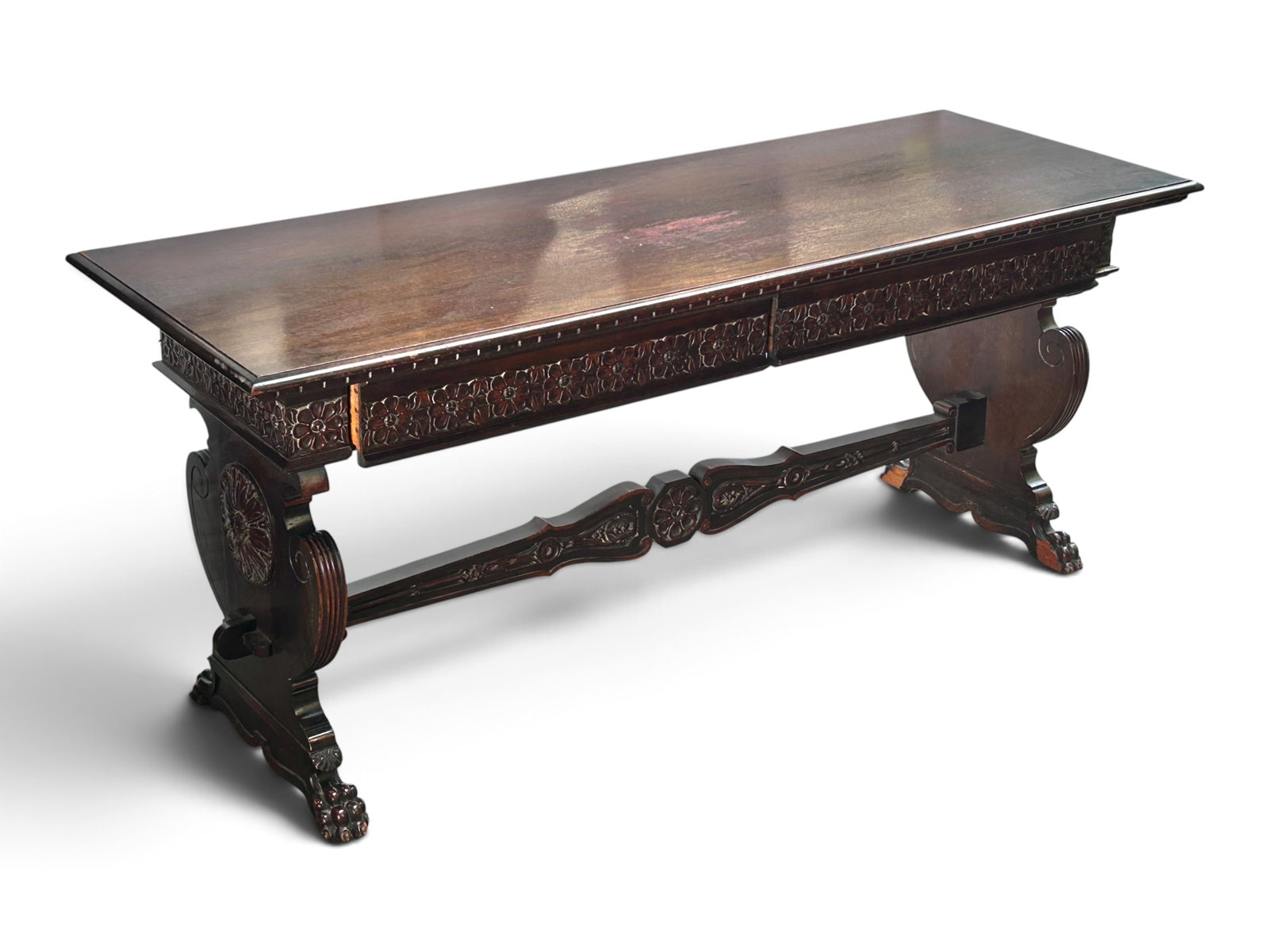 Antique Carved Paw Foot Library Table or Console.: The dark wood table has carved trestle legs with scrolls, a medallion, and paw feet on the front and back. It has two drawers which have relief carvings of flowers, and a stretcher with a central