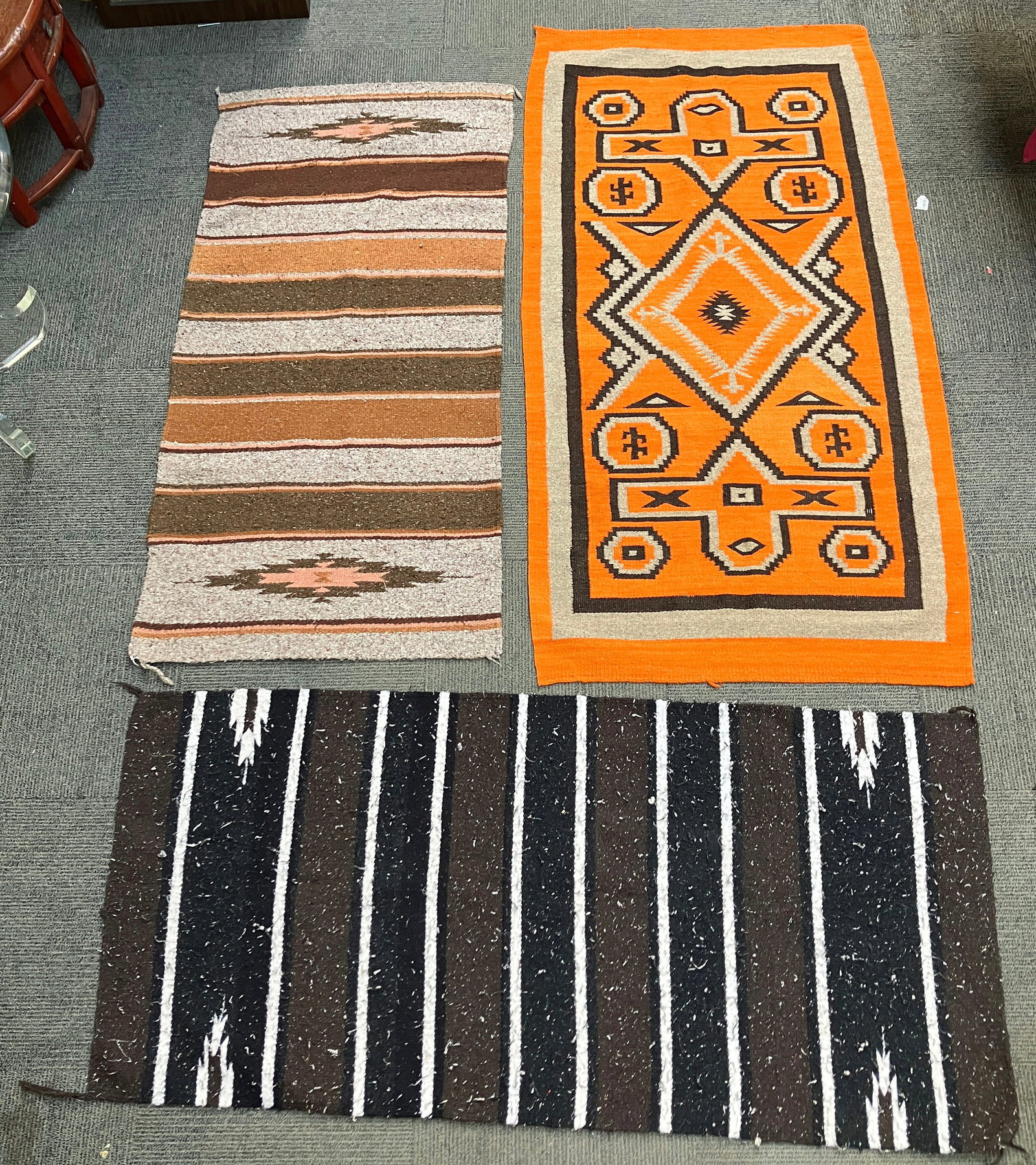 Lot of 3 Navajo Style Rugs.: They could use a cleaning. One of them resembles a J.B. Moore variant. The largest item measures 65 1/2" x 31". The smallest item measures 28" x 57 1/2". In-house shipping is available. To receive the