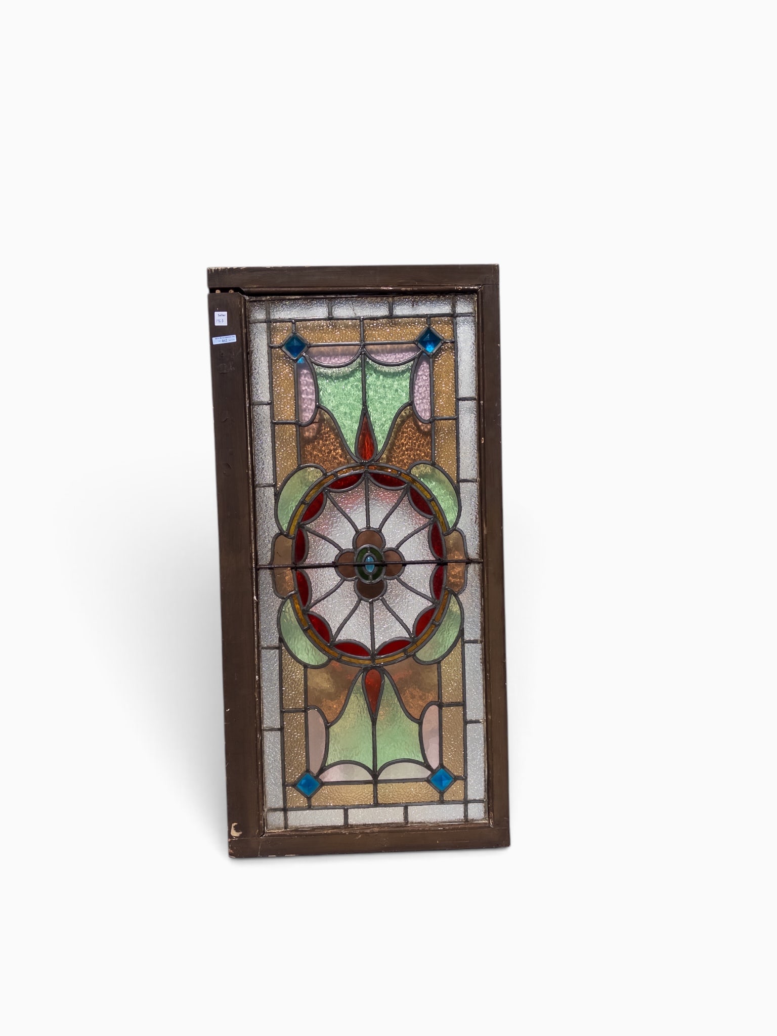 Victorian Leaded & Stained Glass Window.: The textured stained glass transom window has a symmetrical design with a central flower design and a multifaceted blue jewel near each corner. The dark wood frame measures 22" x 45". One side of the