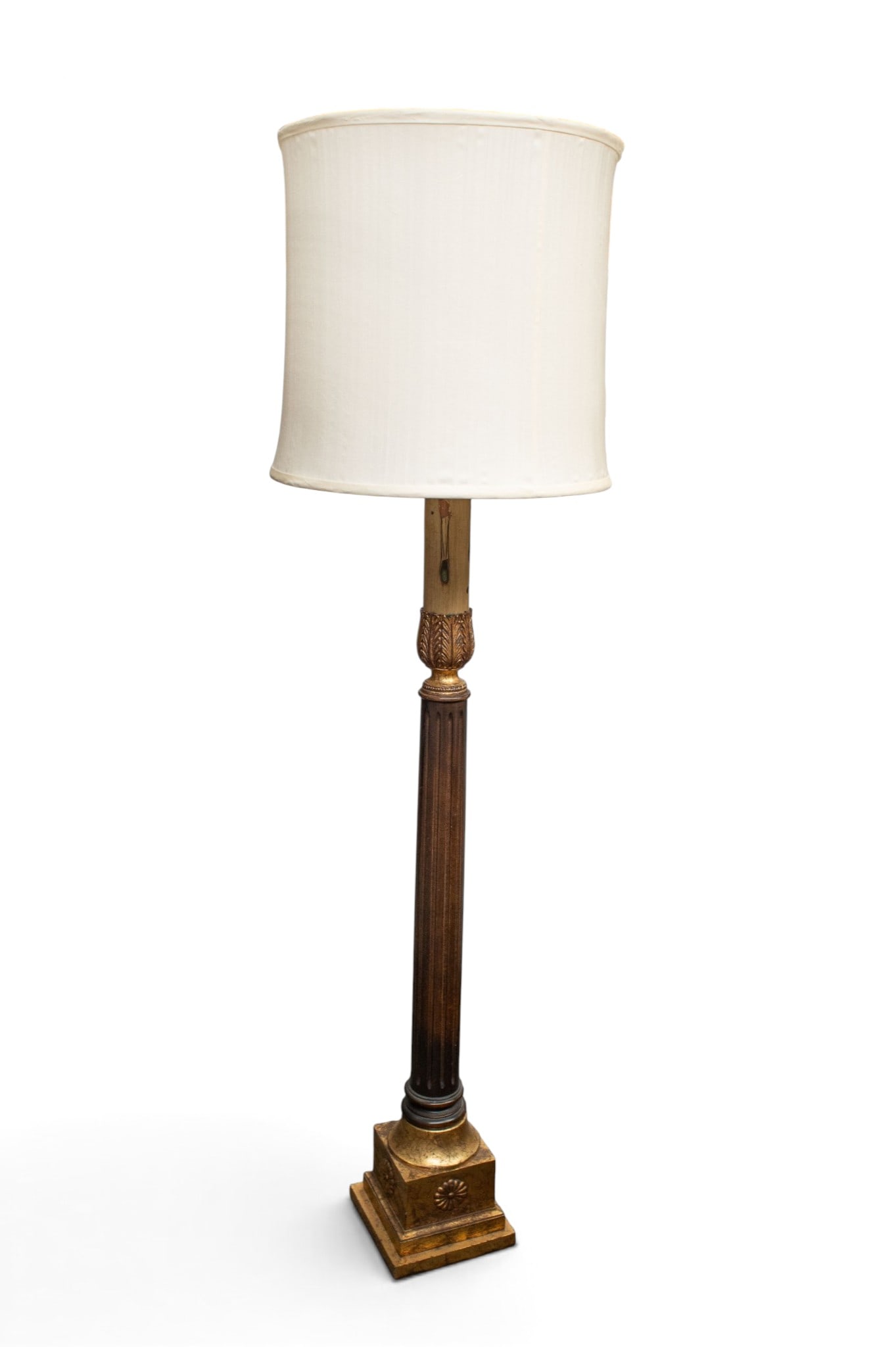 Carved Neoclassical Style Floor Lamp.: The lamp has a carved base with a tiered square bottom having flower carvings. It has a column-style post, and gilded foliage designs above the column. The white lampshade is damaged. It measures 63 1