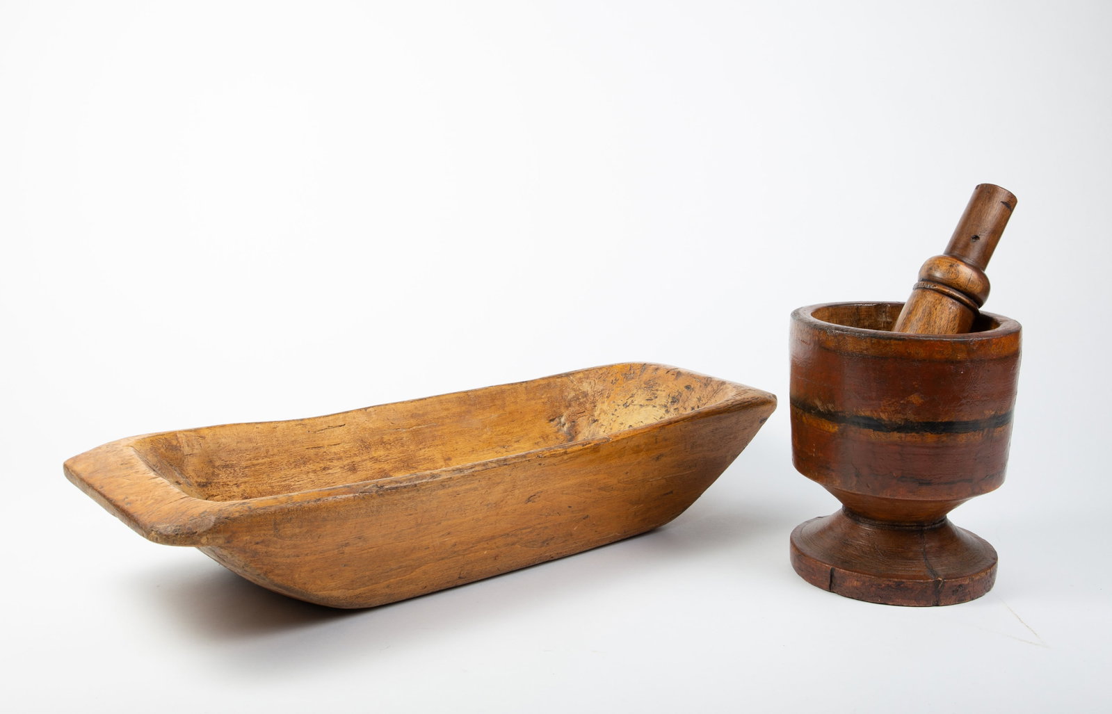 Primitive Dough Bowl & Carved Mortar and Pestle.: The lot contains 2 old carved wood items. The light wood dough bowl measures 6" x 30 1/2" x 11 1/4". The mortar and pestle has a pedestal base and some painted band details. The mortar measures 10