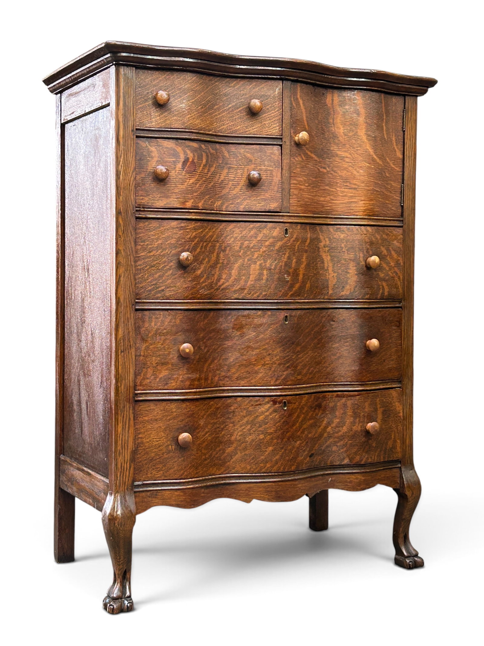 Antique Tiger Oak Chest.: This chest or dresser has a serpentine front with five drawers, one door with an inner storage compartment, wood knobs, and carved front feet. Overall, it is in good condition, with some minor wear.