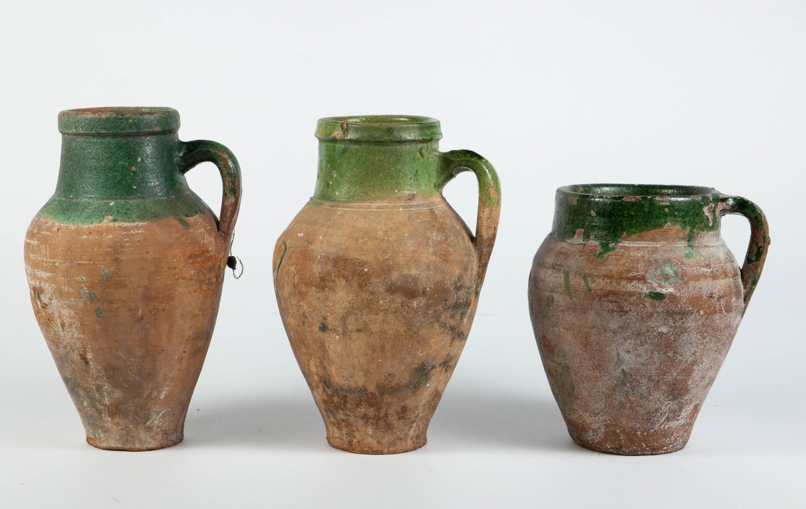 Set of 3 Terracotta Oil Jar Jugs.: Their age is unknown. They have a fair amount of surface wear, but still present well overall. The largest one measures 7 1/4" x 6 3/4" x 11". The smallest jug measures 7 5/8" x 6 5/8" x 8 12". In-hou