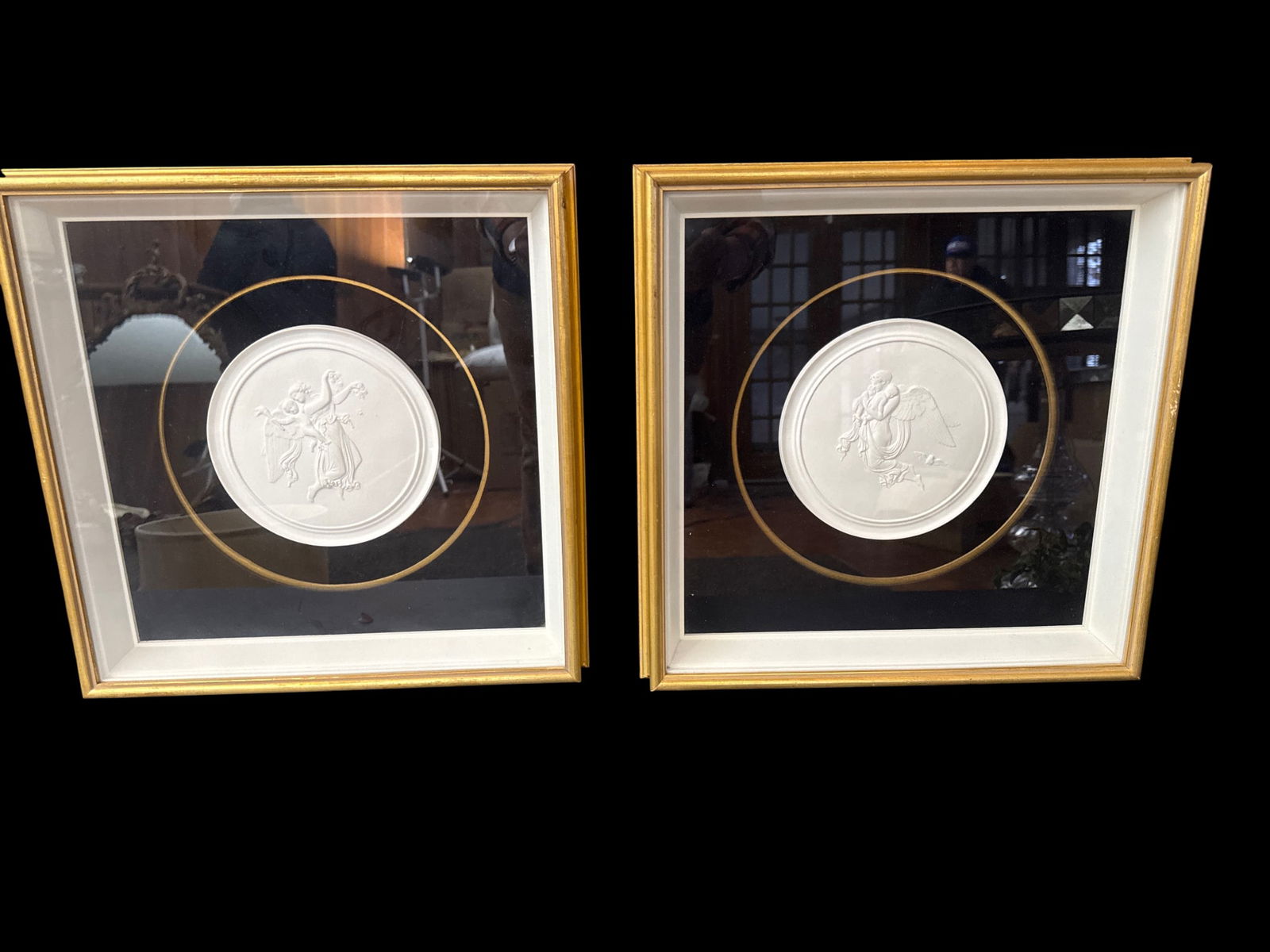 Pair of Neoclassical Bisque Porcelain Relief Medallions of Putti, Shadowbox Framed, 15" H: A decorative pair of Neoclassical-style bisque porcelain relief medallions, presented in matching shadowbox frames. Each work centers on a circular, unglazed white porcelain medallion modeled in low r