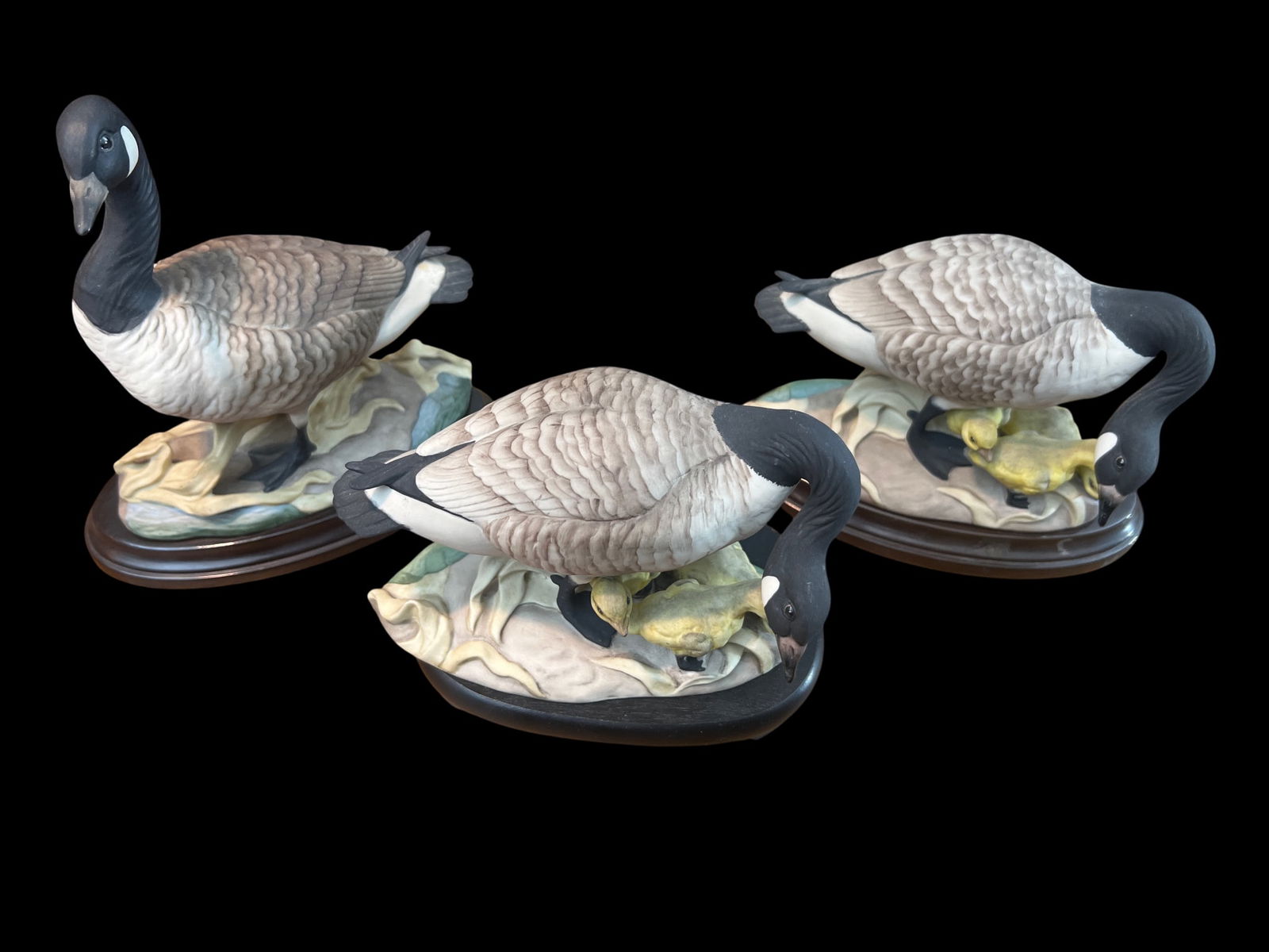 Collection of Three Boehm Porcelain Canada Geese with Goslings #408, USA, 8": Three Boehm Canada Geese figurines from #408 series, each mother goose with 2-3 yellow goslings. Bisque finish, hand-painted naturalistic colors. White chin strap marking, marsh vegetation bases. Hors