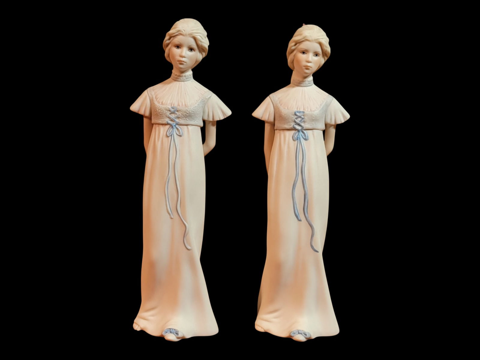 Pair of Cybis Studio Bisque Porcelain Female Figures in Regency Taste, Signed, 9" H: A matched pair of Cybis Studio American bisque porcelain figures modeled as young women in Regency taste, likely late 20th century. Each stands in a softly draped, columnar gown with short flutter sle