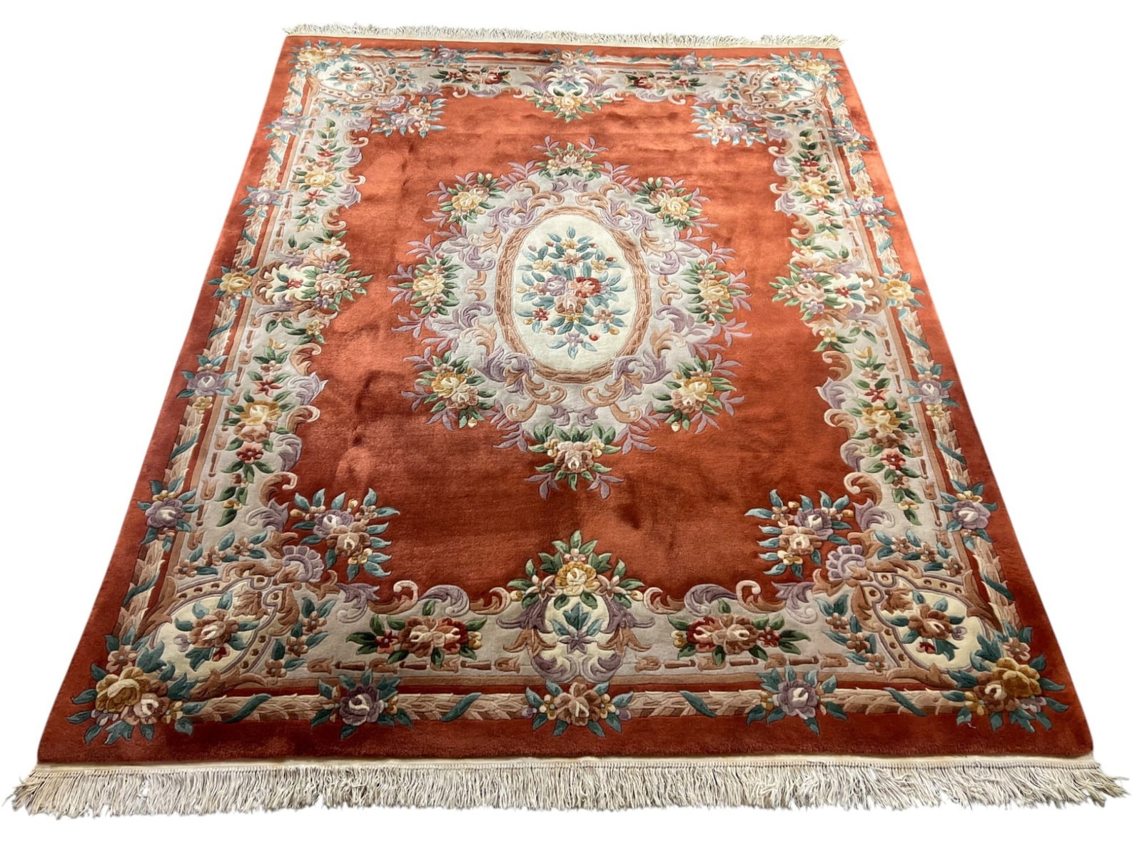 Chinese Aubusson-Design Wool Rug, 8′ × 10’1″: A room-size Chinese hand-woven wool rug in the French Aubusson taste. A warm rust/terracotta field is centered by a soft oval floral medallion — a bouquet of roses and foliage in ivory, sage green, 