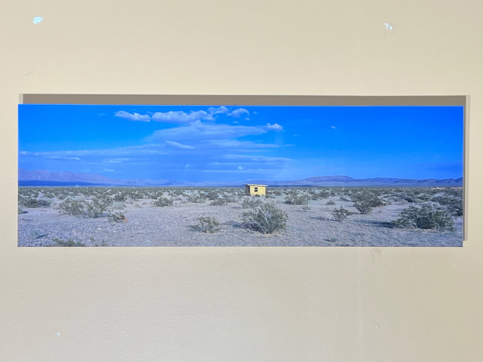Contemporary Panoramic Photograph, Desert Landscape with Lone Cabin Under a Wide Blue Sky, Plexig...: A sweeping panoramic photograph of an arid desert basin beneath an expansive, luminous blue sky. A small, solitary cabin sits near the center of the composition, dwarfed by the vastness around it