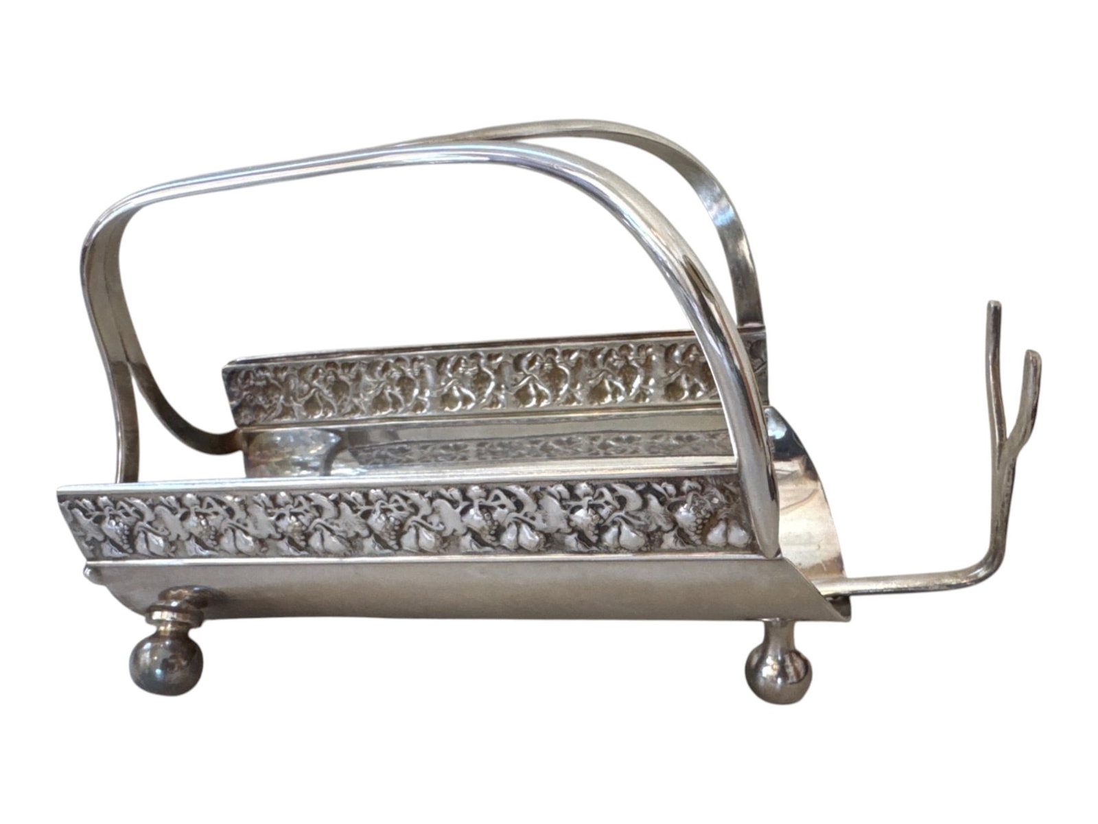Silverplate toast rack with pierced floral borders, 7 in.: Silverplate toast rack or letter holder with a shaped rectangular body, arched carry handle, and four ball feet. The side rails feature repeating pierced floral and foliate ornament, while the curved