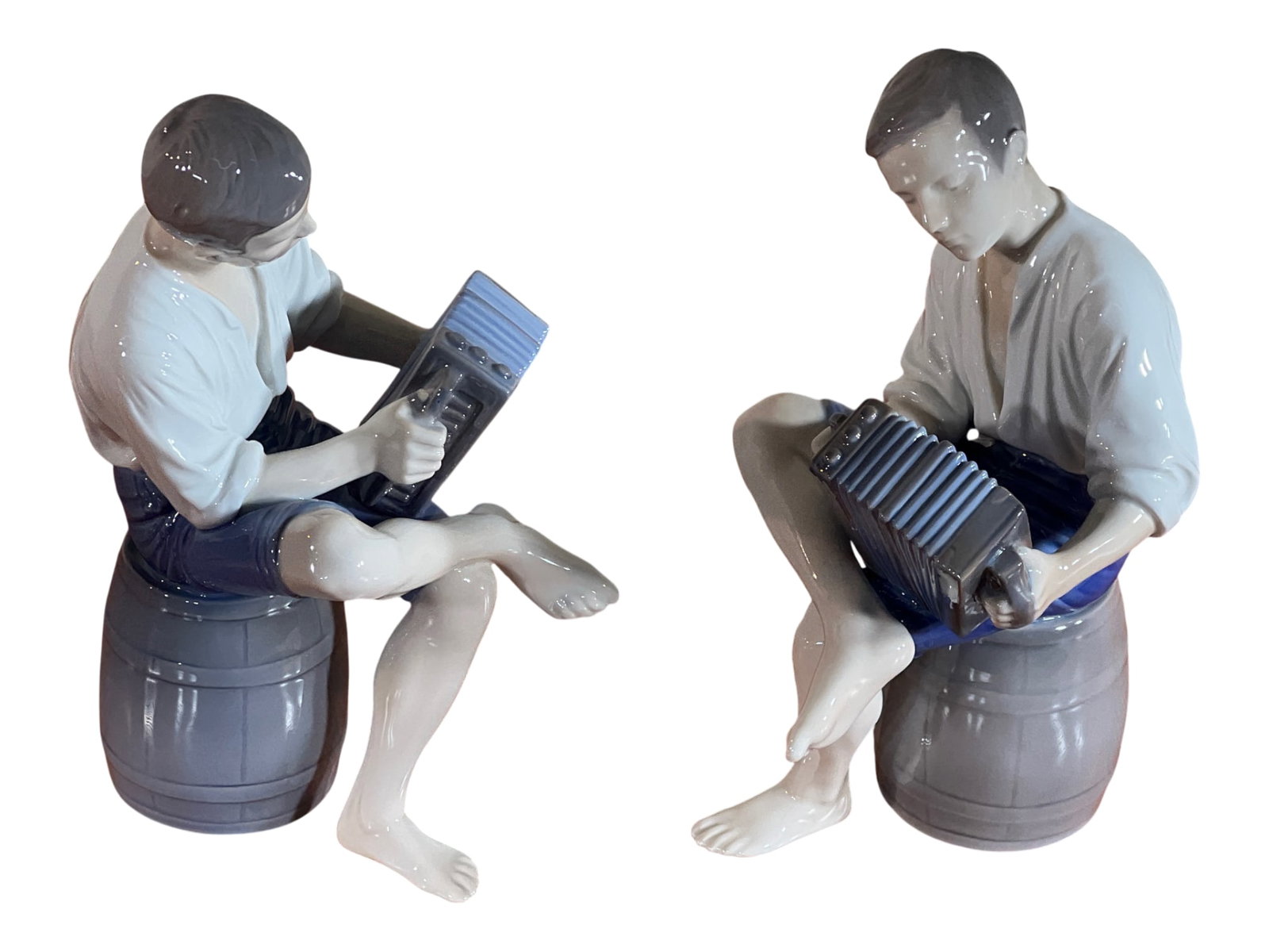 Pair Bing & Grøndahl Danish Porcelain Accordion Players, 9": This delightful pair of Danish porcelain figurines depicts barefoot young men seated on wooden barrels, each playing an accordion in a relaxed pose. Both pieces bear the Bing & Grøndahl factory m