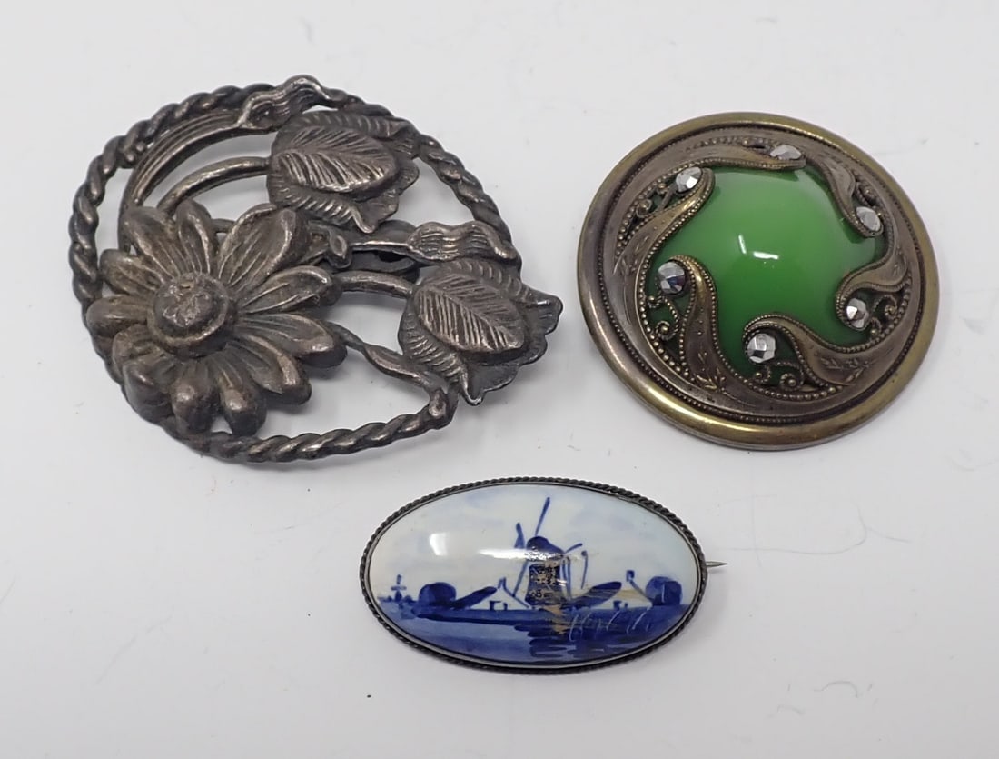 3 Brooches: Includes a vintage oval Delft porcelain pin with a sterling frame, extended pin and c-clasp; plastic floral brooch; and a rosette converted brooch with center green slag glass center.
