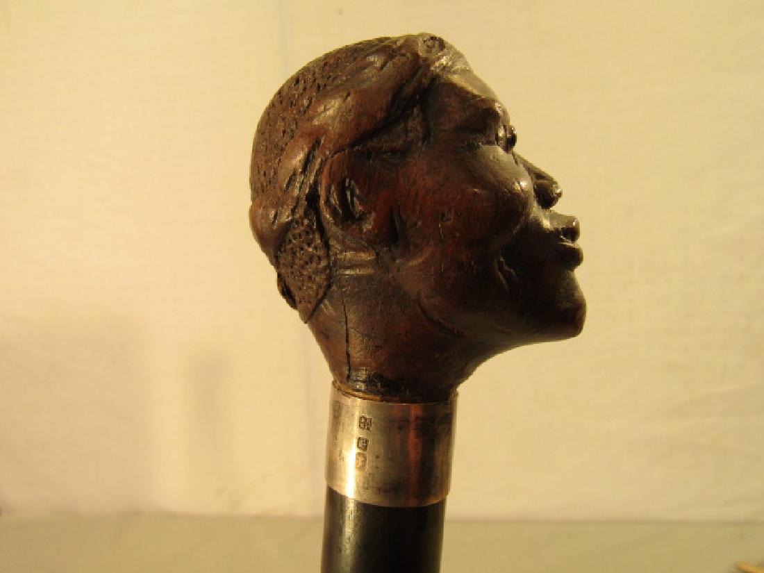 FOLK ART BLACK MAN CANE: Antique English carved wood folk art cane with handle in form of the bust of a black man with glass eyes. Silver collar has London hallmarks and maker WL&S. Ebony wood shaft. Size: 35.5 in long, 2 in