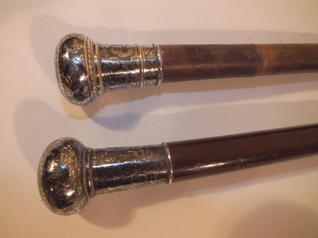 2 ANTIQUE NIELLO SILVER CANES: 2 sterling silver niello head canes with arabesque designs and figures on knob handles, 33 and 35 inches long, bamboo and wood shafts.