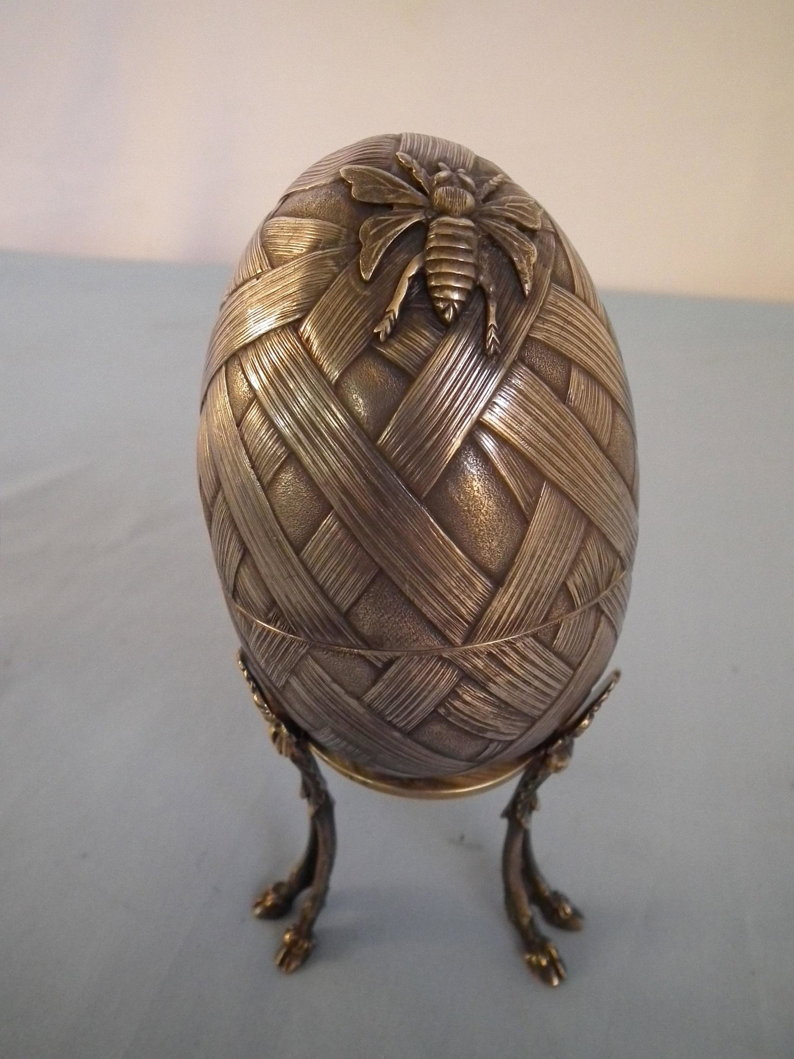 RUSSIAN FABERGE SILVER EGG: Antique Faberge Russian silver egg on stand with hoof feet, egg has woven design with bee. Egg is 4 in high, stand 3" tall. Has gilt inteiror and 84 silver standard mark with Faberge marks. 7.9 ozt.