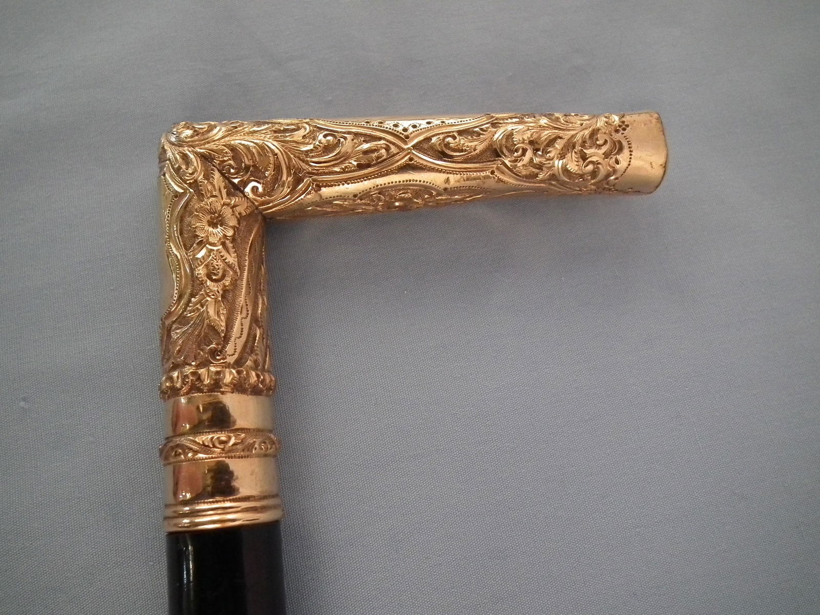 GOLD PLATED CANE: Antique gold plated elaborately engraved cane with ebony shaft, 3.5 in handle, floriform designs, silver plated ferrule. 36.75 in long.