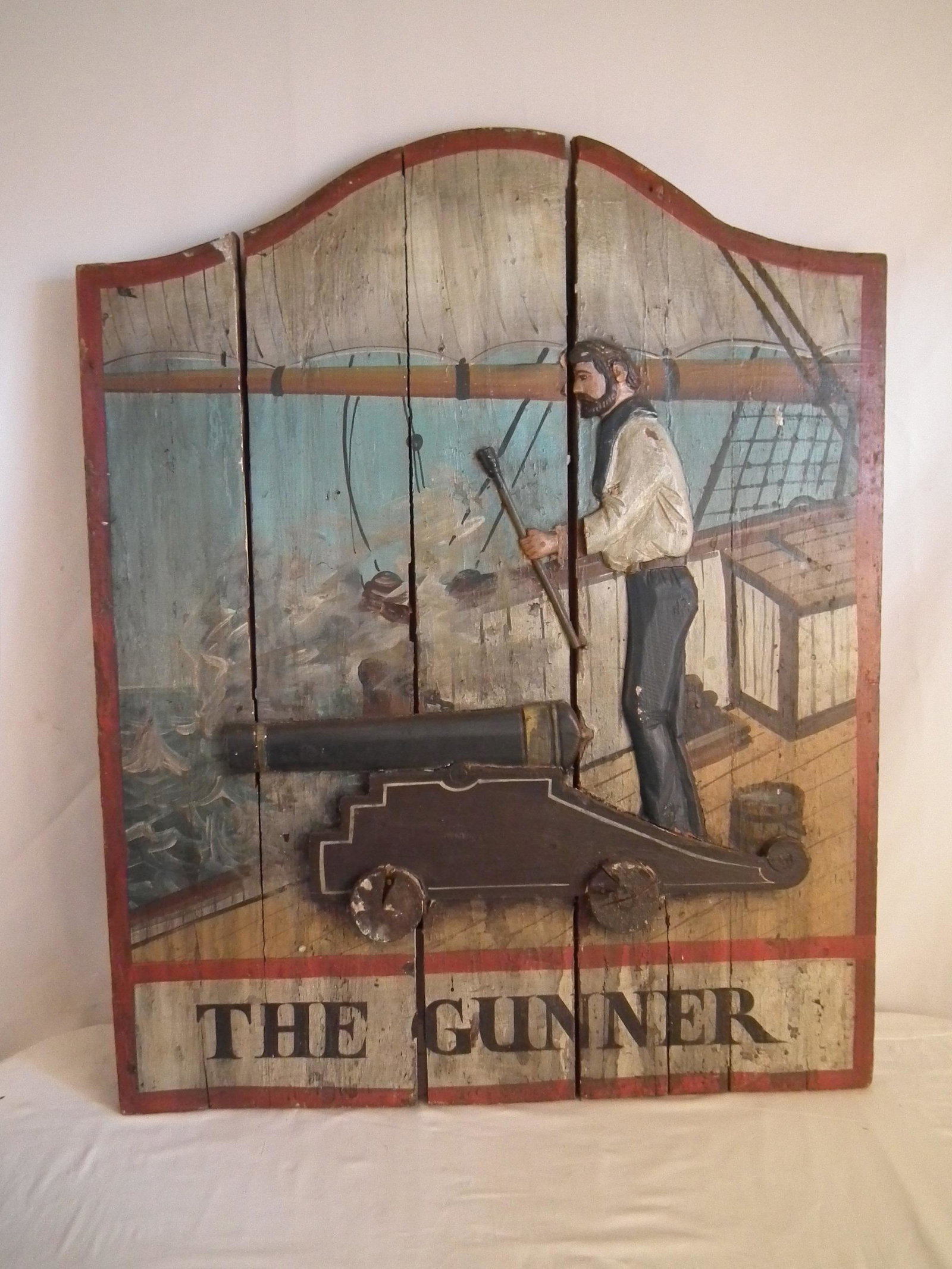 WOOD SIGN THE GUNNER: Old painted and carved wood 3 dimensional sign of a sailor on ship firing a cannon titled THE GUNNER. 41 x 33 inches.