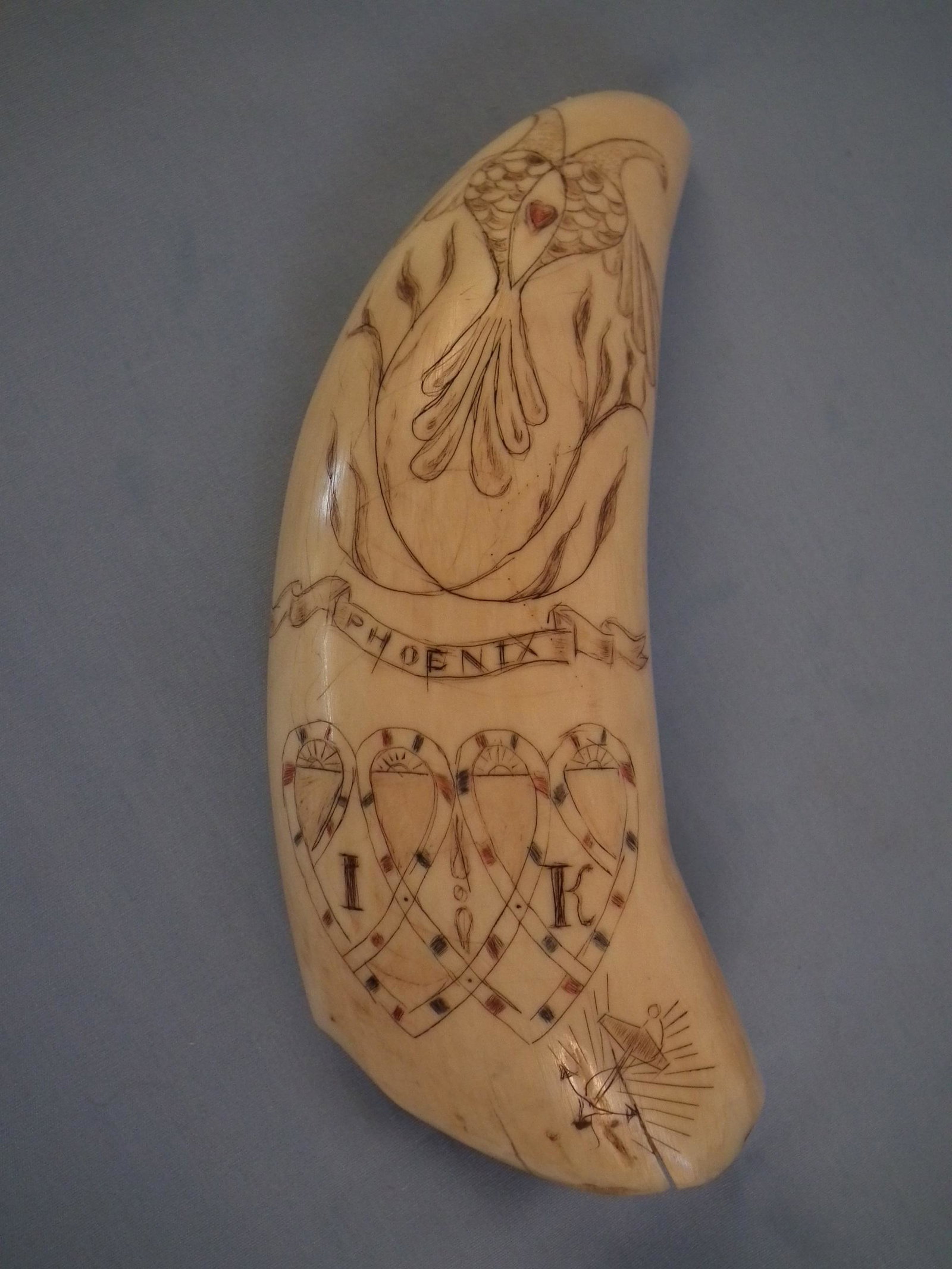 SCRIMSHAW WHALE TOOTH - WHALE SHIP: 19th century whale tooth with colored scrimshaw of a whale ship on one side and PHOENIX verso with flanking birds, hearts, anchor and initialed IK. Size: 6.5 in high, weighs 12.2 oz.