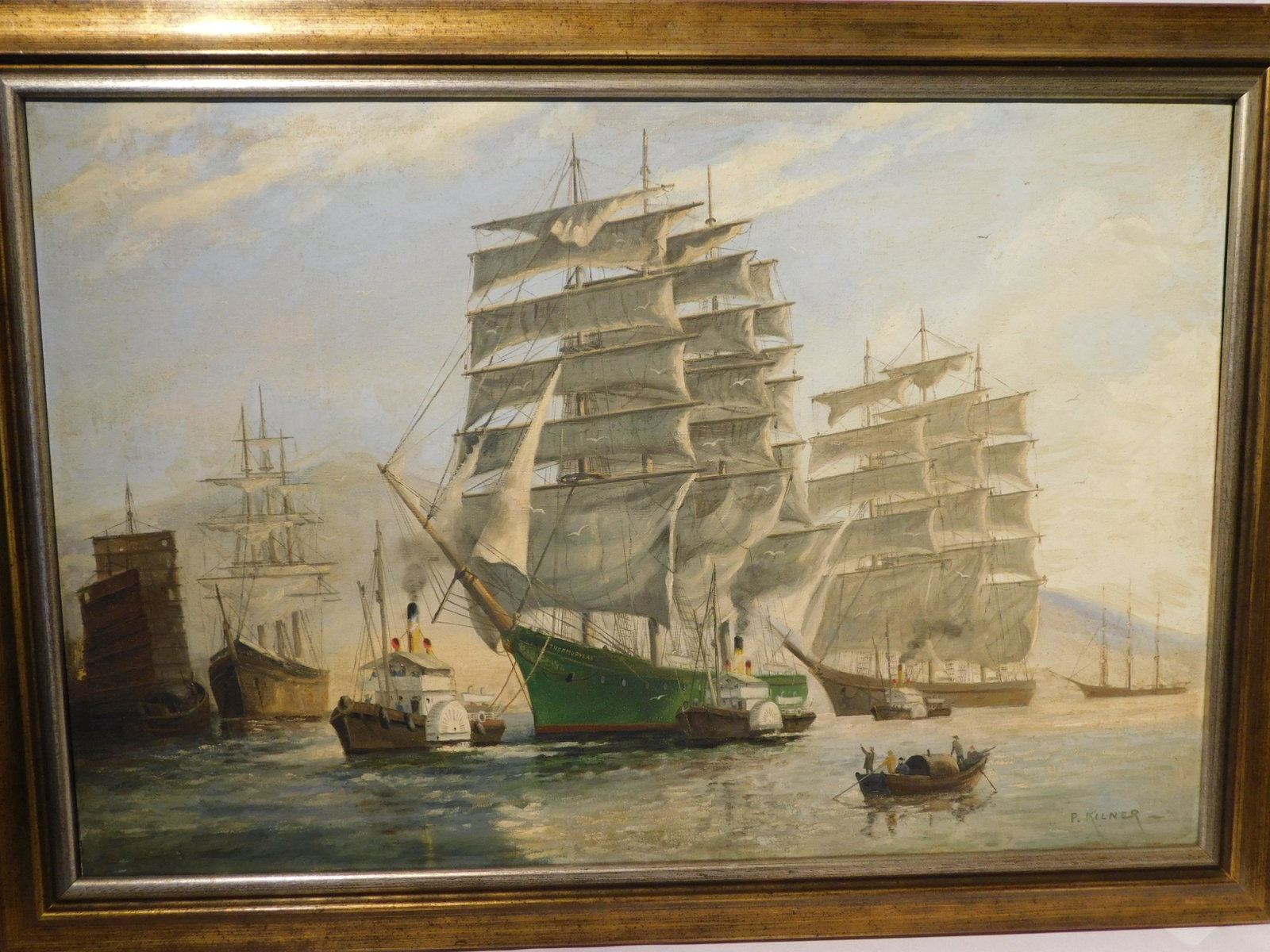 KILNER PAINTING OF SHIPS IN HARBOR: Antique oil painting on canvas depicting the ship THERMOPYLAE in foreground with other ships and figures. Signed P. Kilner. 20 x 30 inches, framed 24 x 34. Good condition with repaired tear. (Philip K