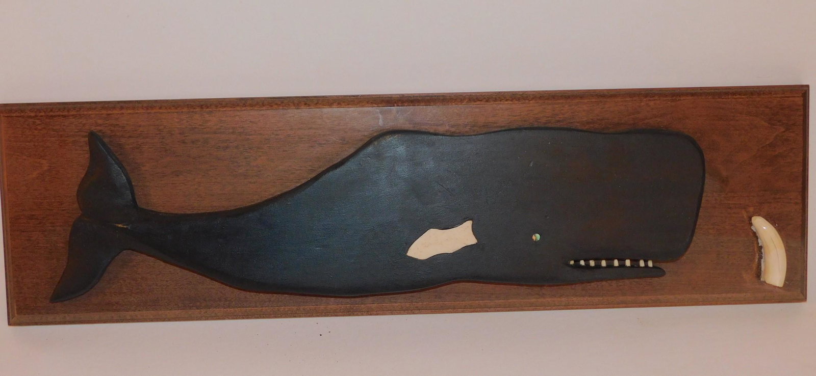 CARVED WOOD WHALE PLAQUE: Vintage wood plaque with carved sperm whale with inlaid whale bone and small whale tooth. 22 x 6 inches. Buyer is responsible for pickup or removal of whale products in accordance with Federal and Sta