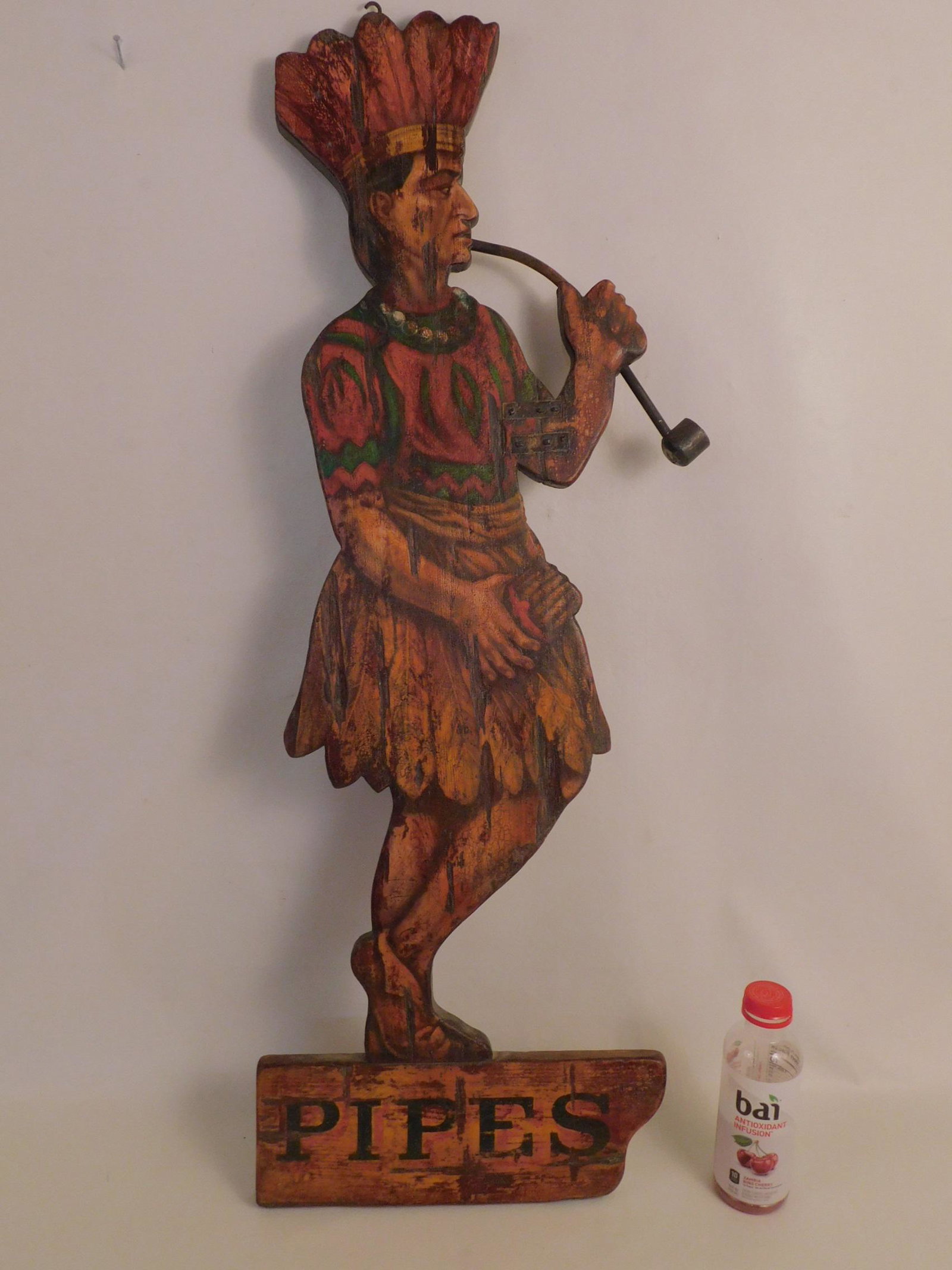 TOBACCO WOOD PAINTED SIGN - INDIAN: An old painted and carved wood tobacco sign in form of a Native American Indian smoking a pipe with word PIPES. 41 in high and 13.5 in wide.