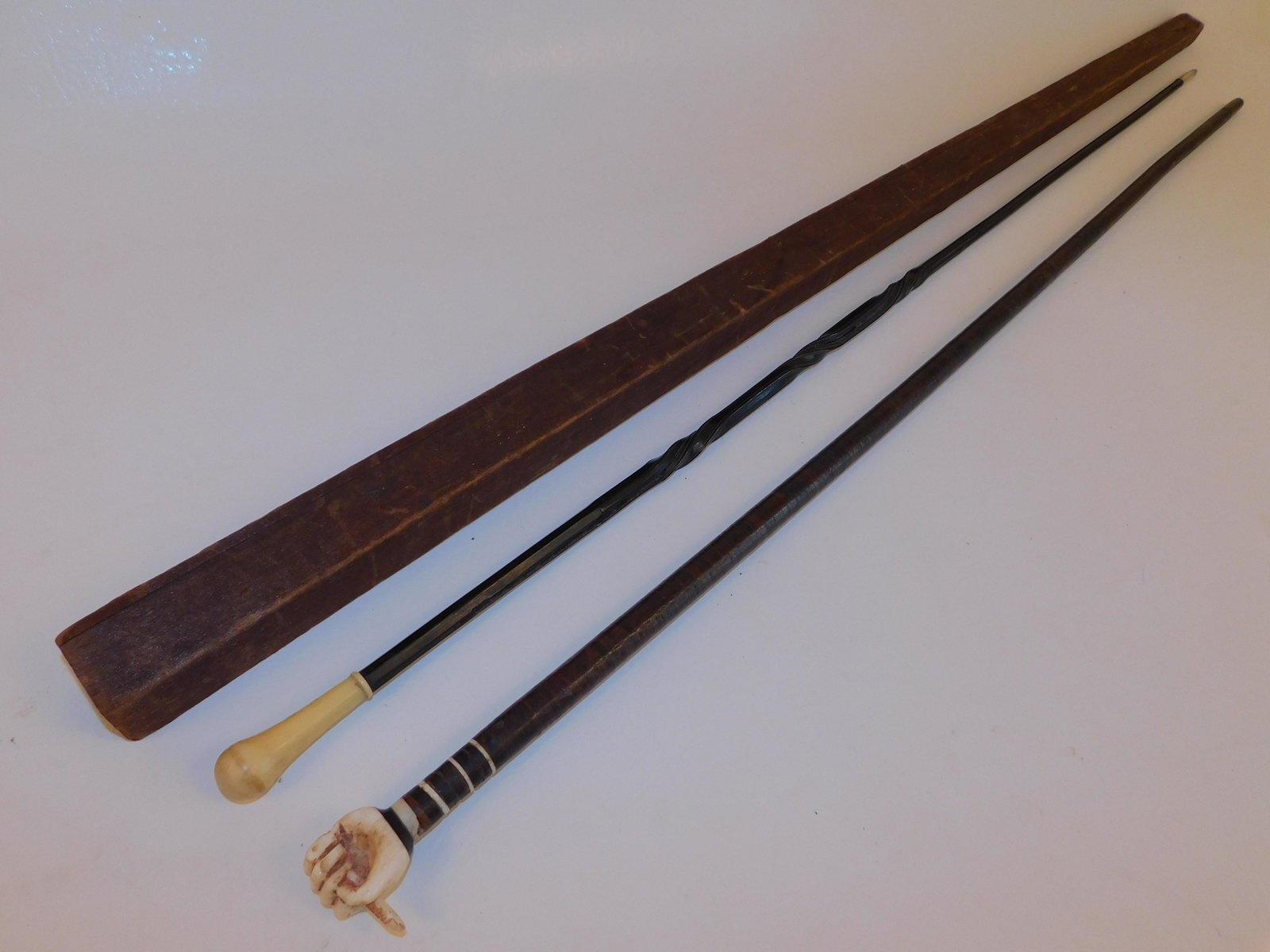 2 PLANTATION CANES: 2 antique plantation canes: flexible leather-wrapped shaft with carved bone fist holding snake handle, 34 inches; and a baleen flexible whip cane with small bone knob, silver ferrule, and original woo