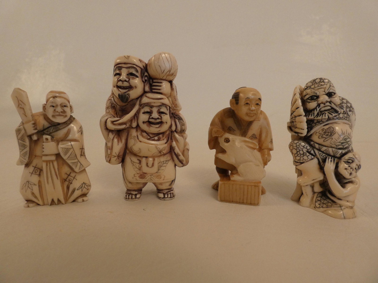 4 JAPANESE NETSUKES: Lot 4 old Japanese carved bone netsukes to 2.75 in tall: 2 men with mallet; man & rabbit; man with fan, signed; man with implements, signed.