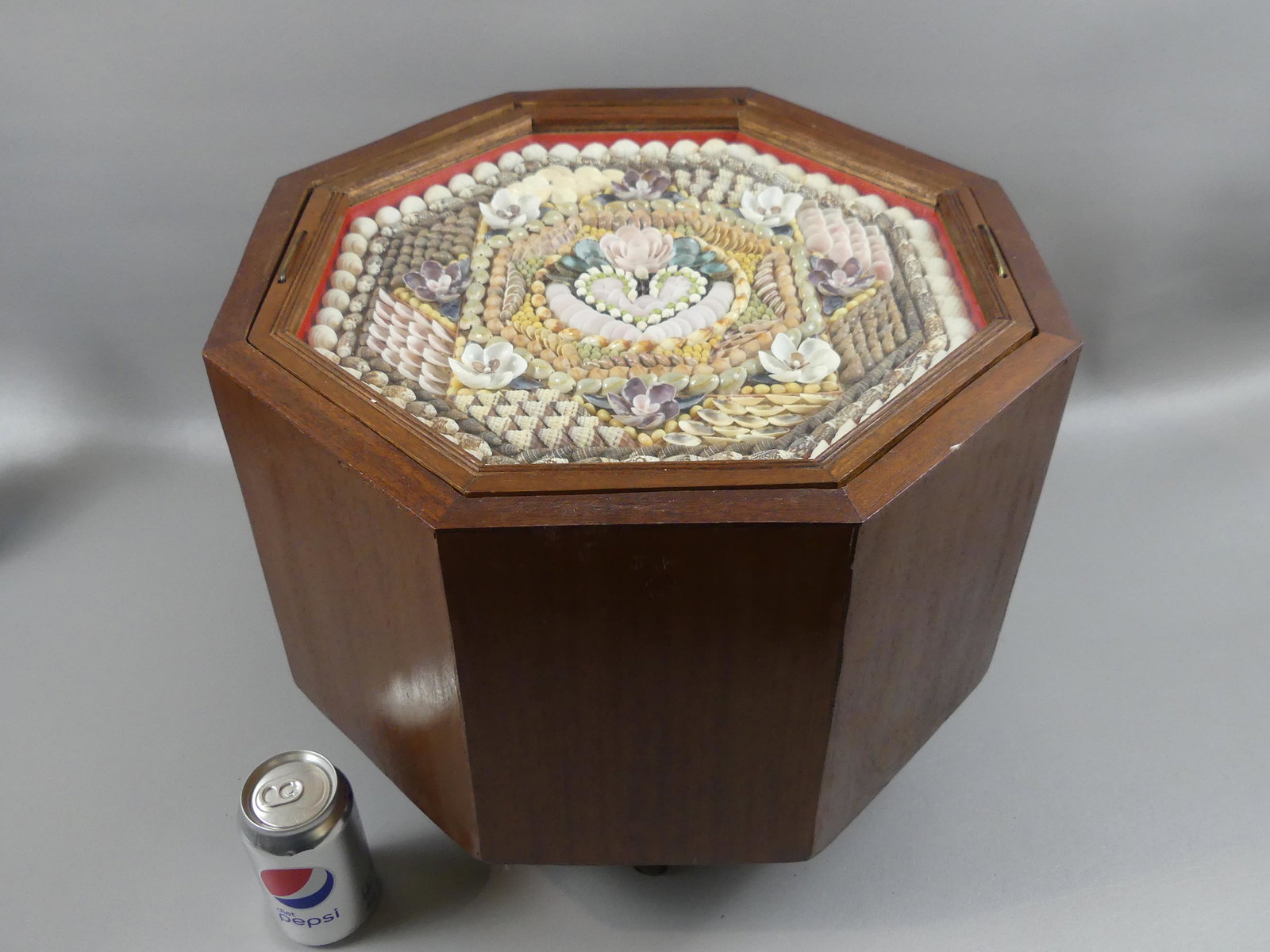 OLD SHELL VALENTINE FOOTED BOX: Old octagonal framed seashell valentine with handles, mounted in a walnut octagonal storage box or chest with turned legs and brass handles. Valentine is 15 inch diameter, box is 18 in diam by 14.5 hi