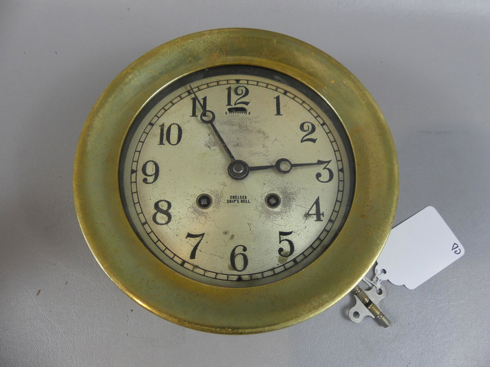 CHELSEA SHIPS CLOCK: Old Chelsea brass cased ship's wall clock with time and strike and 6 in dial (3.5 in deep). Clock is running and striker moves but does not chime so needs adjustment and/or cleaning. Some wear to silv