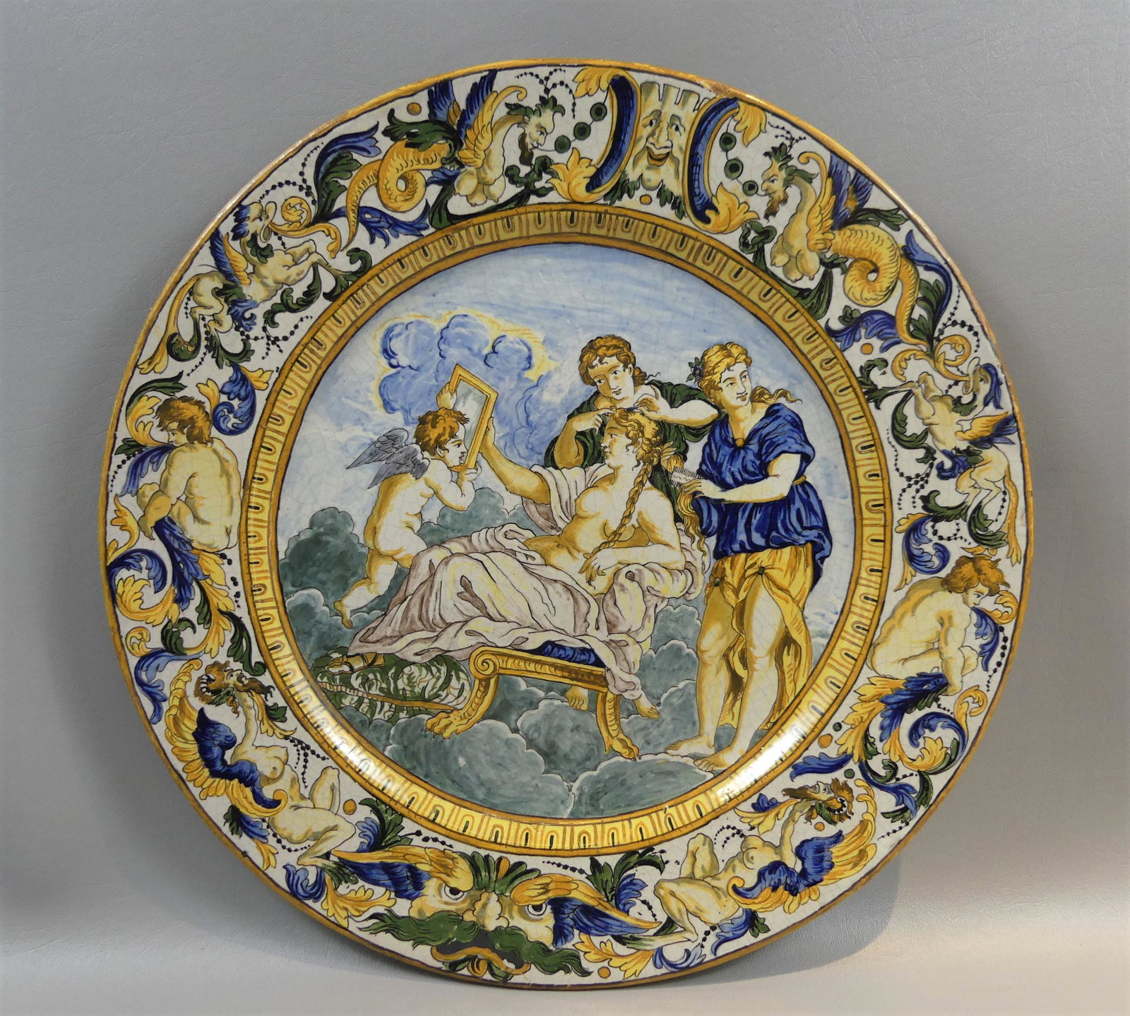 ITALIAN FAIENCE CHARGER - CHERUB & MAIDEN: Antique Italian faience charger with classical scene of cherub and maiden peering in mirror. 16.25 in diameter, no marks. One minor glaze flake on rim.