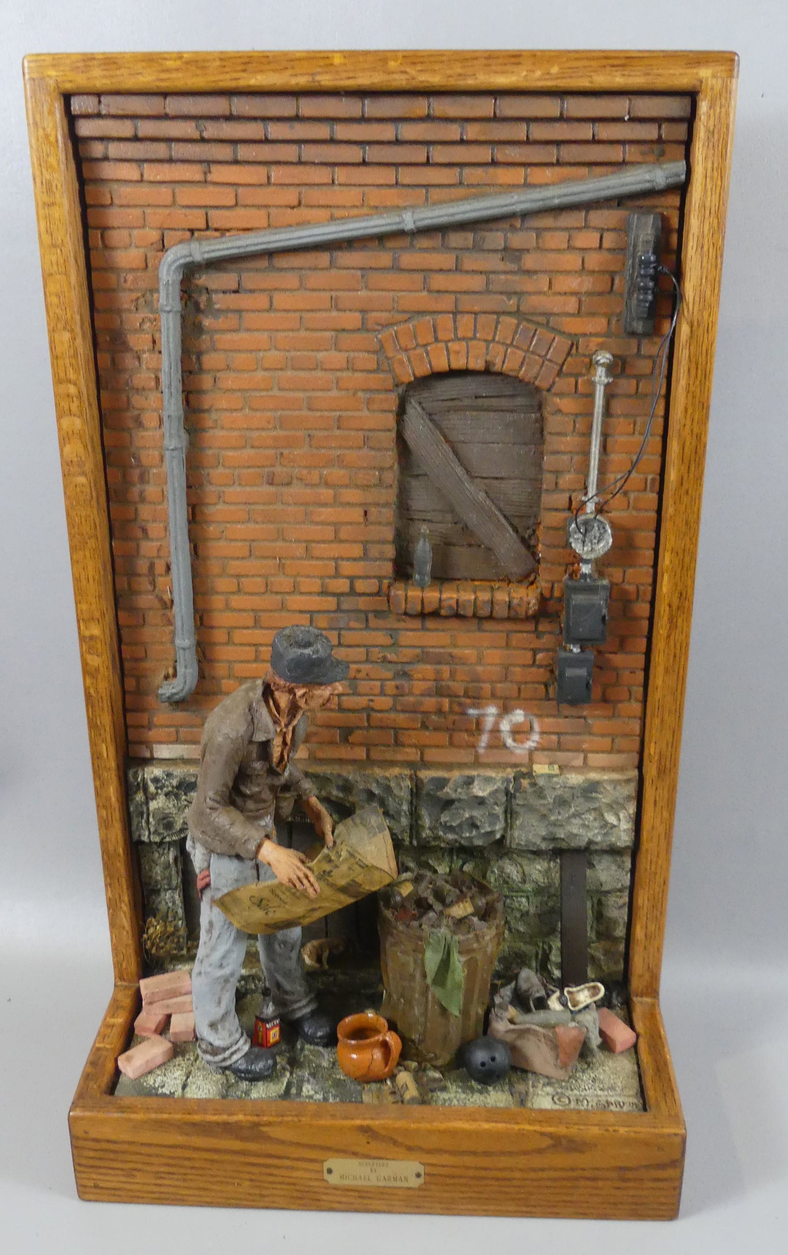 MICHAEL GARMAN 1984 SCULPTURE: Interesting mixed material, folk art shadowbox sculpture depicting a homeless man reading the newspaper in an alleyway. Signed Michael Garman '84. Many authentic details. Size: 27 in high x 15 x 8 in 