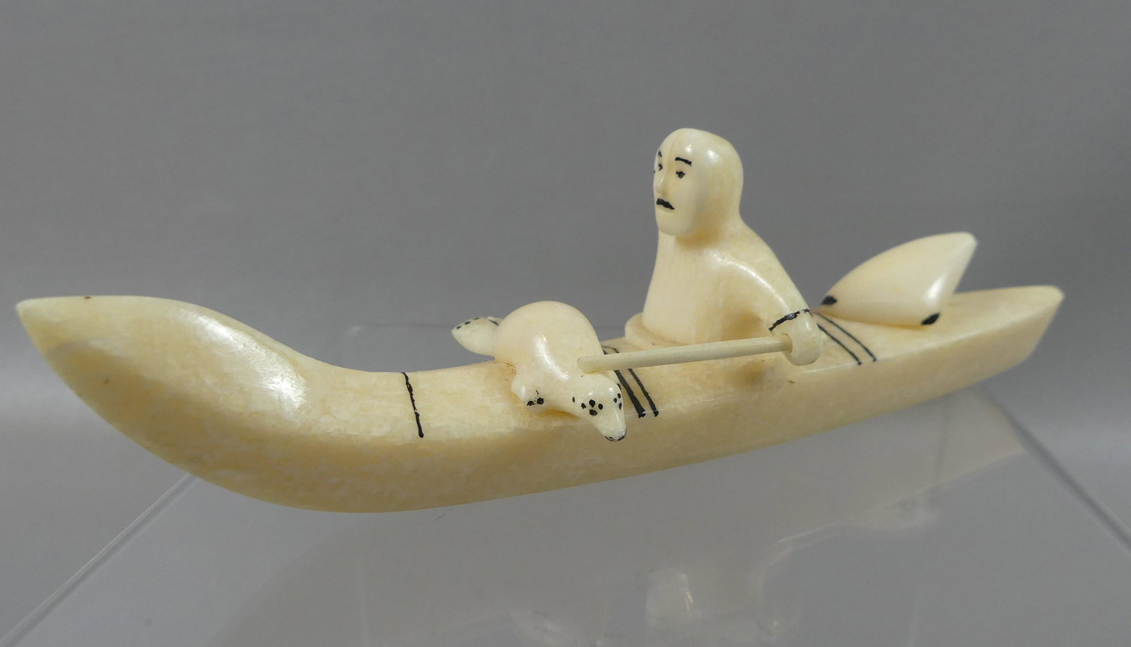 J. KOKULUK INUIT KAYAKER: Carved Inuit walrus bone figure of an Eskimo in kayak with a seal signed John Kokuluk (Alaska artist). 6.5 in long by 1.75 high.