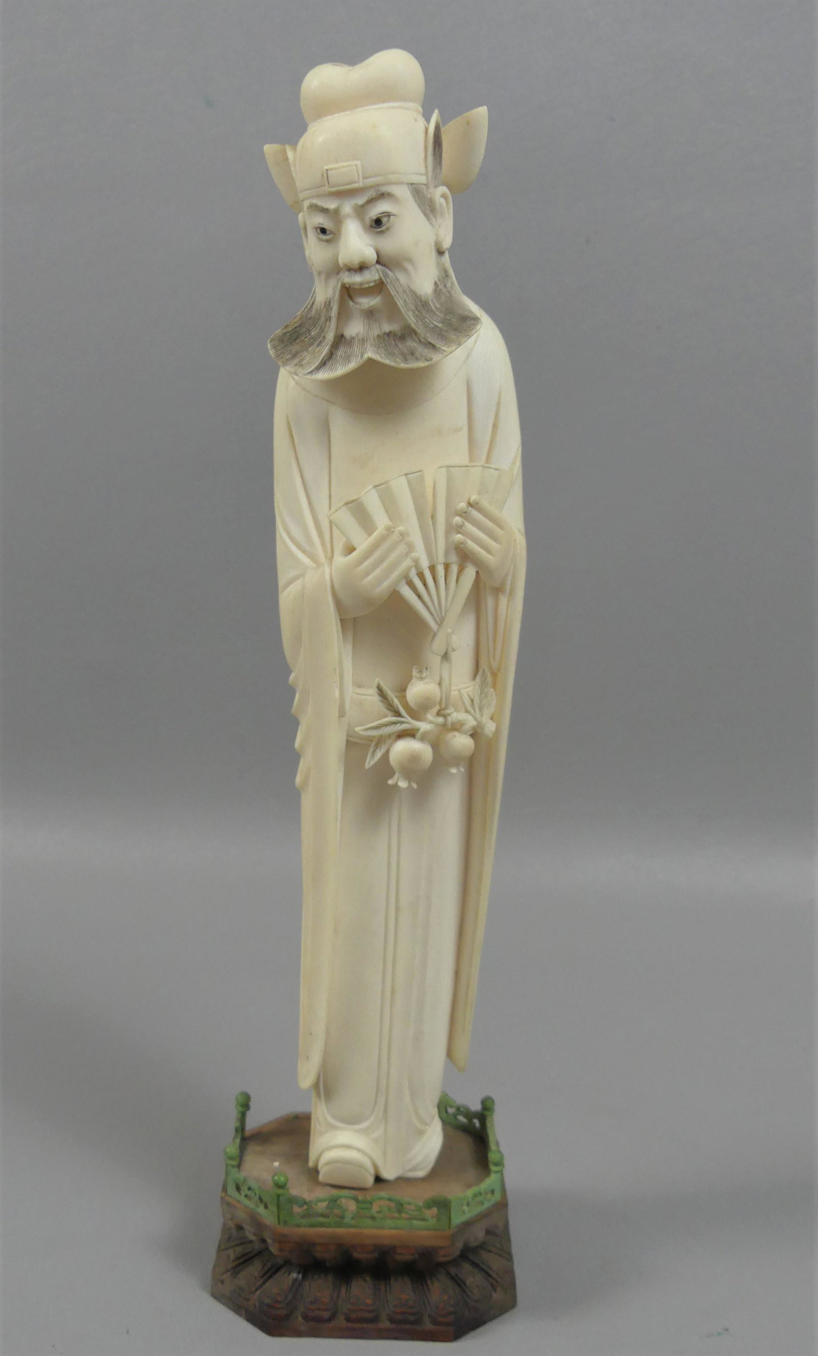 ANTIQUE ASIAN BONE FIGURE OF MAN: Fine antique carved bone Asian figure of a bearded man holding pomegranites and fan. 11.5 in overall on 1 in wood stand. VG condition, minor loss on base. Age toning to back.