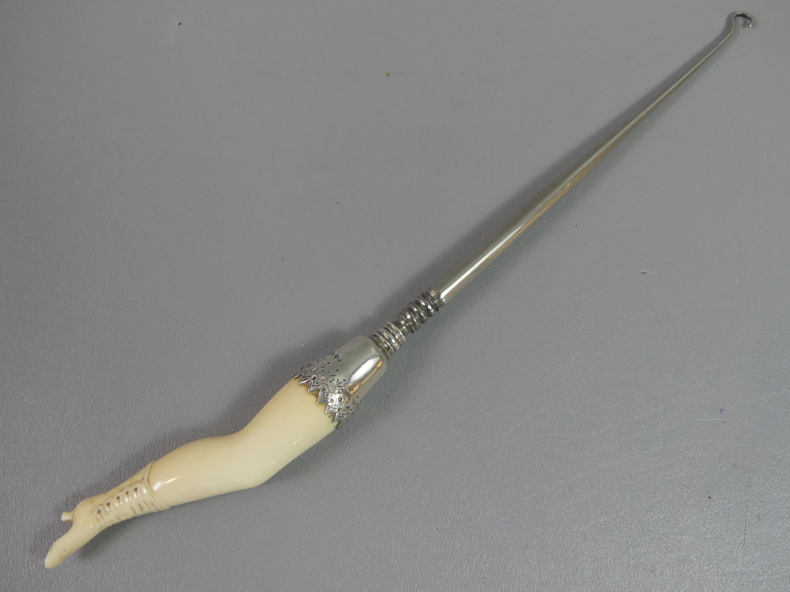 1888 SILVER & BONE BUTTON HOOK - LADY'S LEG: Rare English sterling silver mounted, long button hook with carved bone lady's leg with shoe handle. Hallmarks of Charles Boyton, London, 1888/89. 12.5 in long.