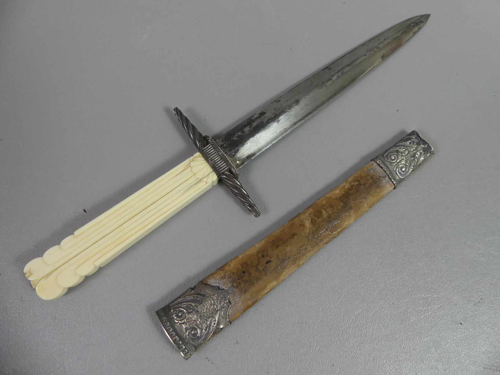 ANTIQUE BOWIE KNIFE: 19th century continental bowie knife or dagger with carved bone handle and leather and silver mounted sheath. 12 in long, blade is 7 in. Some discoloration, light rust on blade.