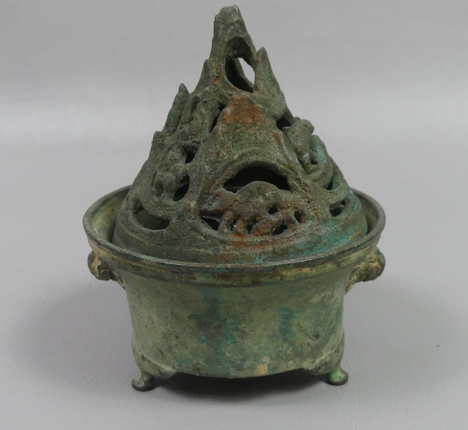 ARCHAIC CHINESE BRONZE CENSER: Archaic bronze Chinese incense burner with 3 feet and reticulated cover having animals on mountainside. Crusty verdigris surface. 4.5 in high x 3.75 diamter. Provenance: Ex-collection of Helga Wall-Ap