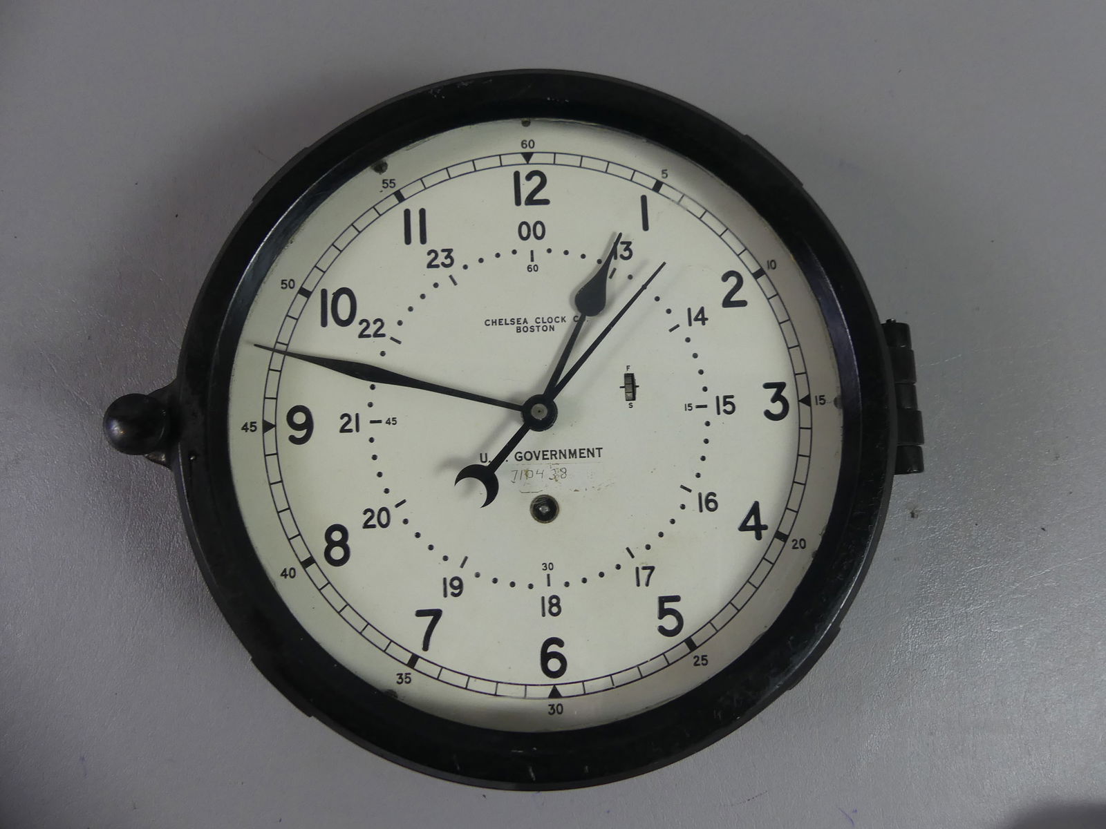 CHELSEA BAKELITE WALL CLOCK: Early/mid 19th century bakelite key wind wall clock by Chelsea Clock Co, dial marked US Government 710438. 9 in across bezel. Has both military and civilian time on metal dial. Untested.