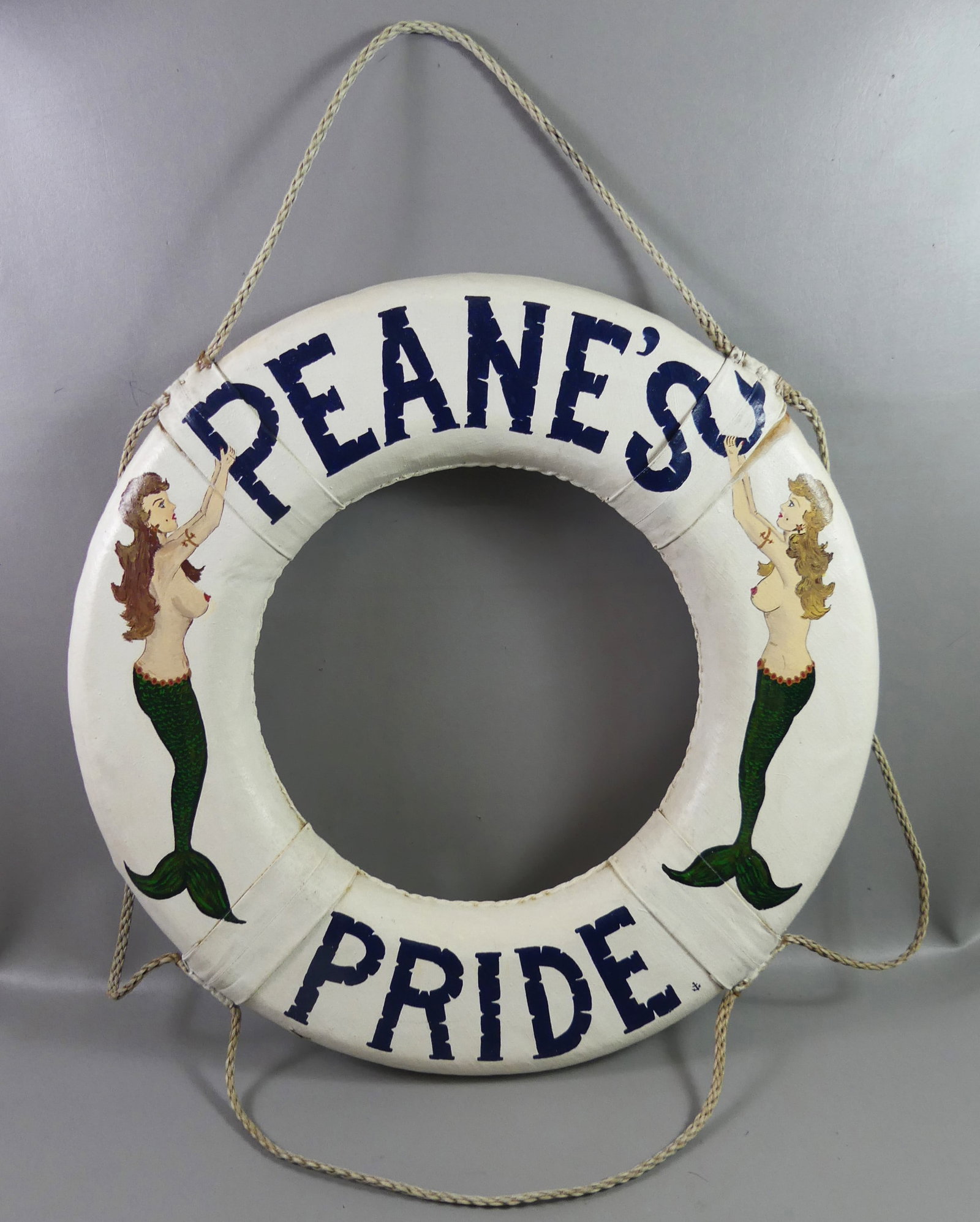 PEANE'S PRIDE LIFE RING BUOY: Old canvas-covered ship's lifesaving ring or buoy with painted mermaids and PEANE'S PRIDE. 30 in diam by 6.5 in wide.