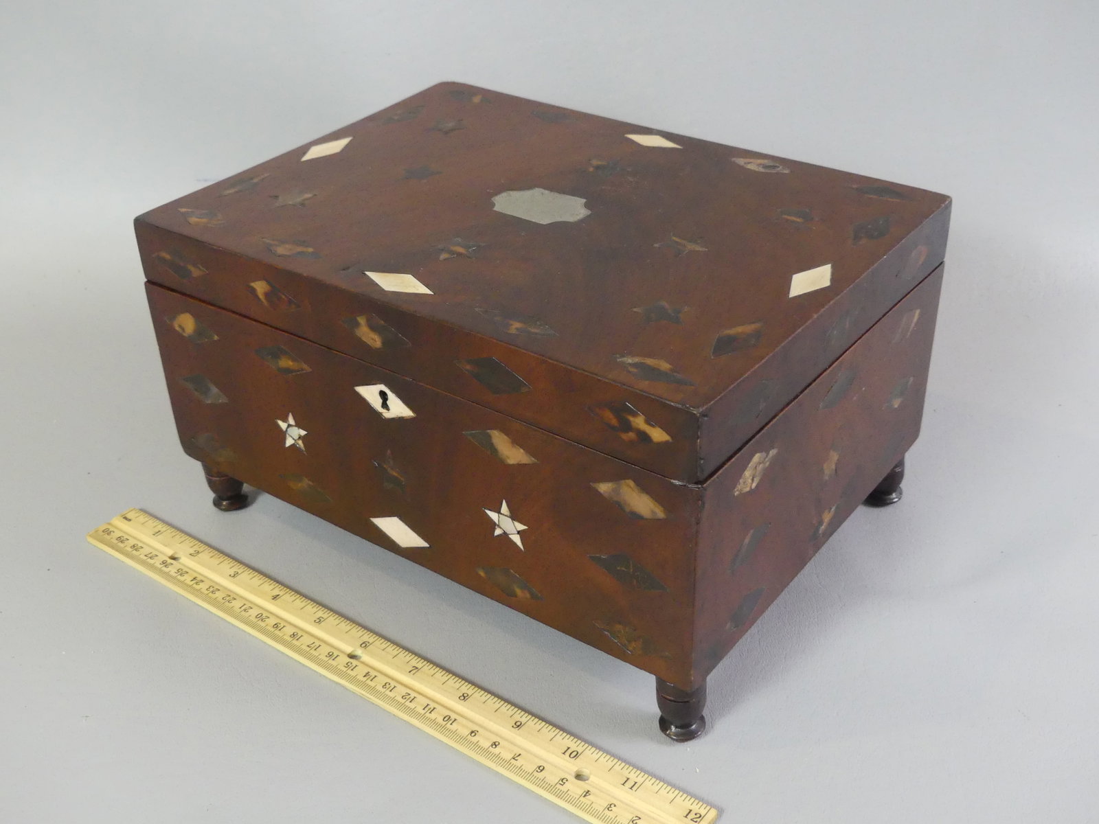 ANTIQUE BONE & SILVER INLAID MAHOGANY BOX: 19th century sailor-made mahogany lift top footed box with inlaid geometric designs (stars, diamonds) in bone, and animal shell with blank silver name plaque. Interior has original mirror (discolored)