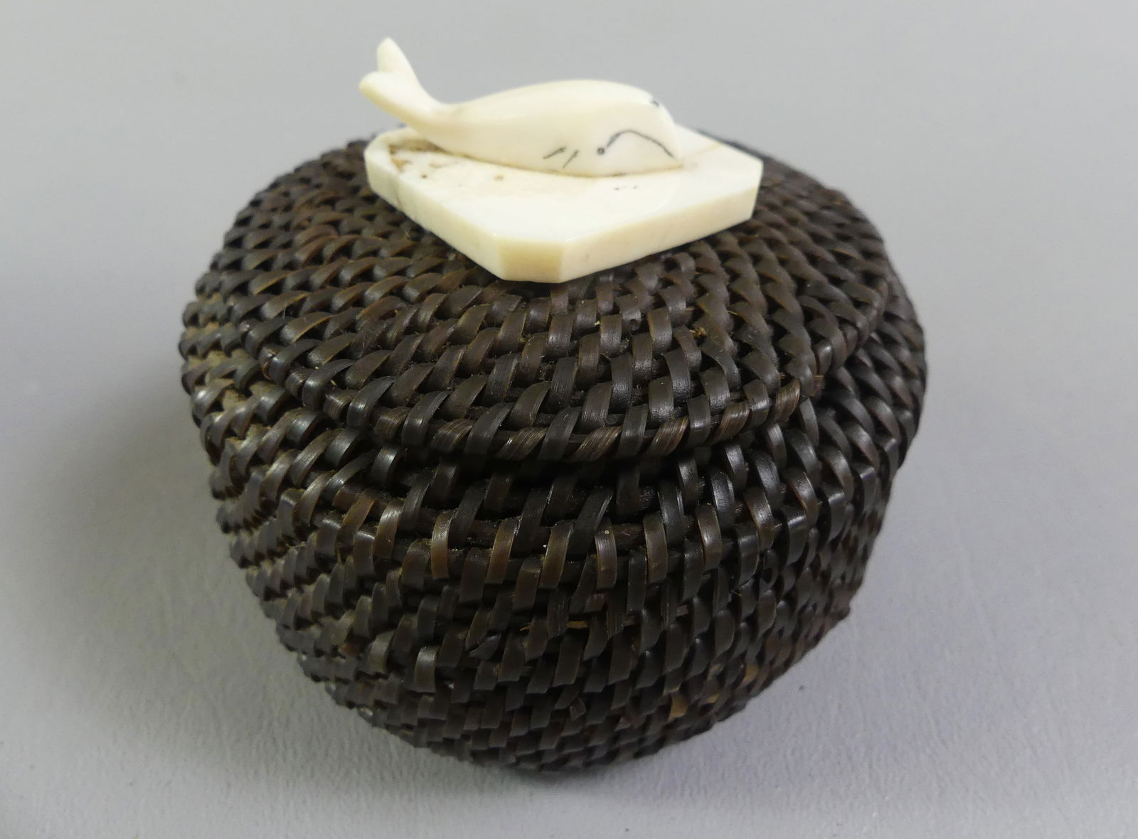 INUIT WOVEN BASKET - KOONUK: Antique small Inuit woven baleen basket with whale bone finial of a whale on lid. Interior of cover signed HK (Note included Made by Hubert Koonuk). 3.5 x 3 inches. VG condition.