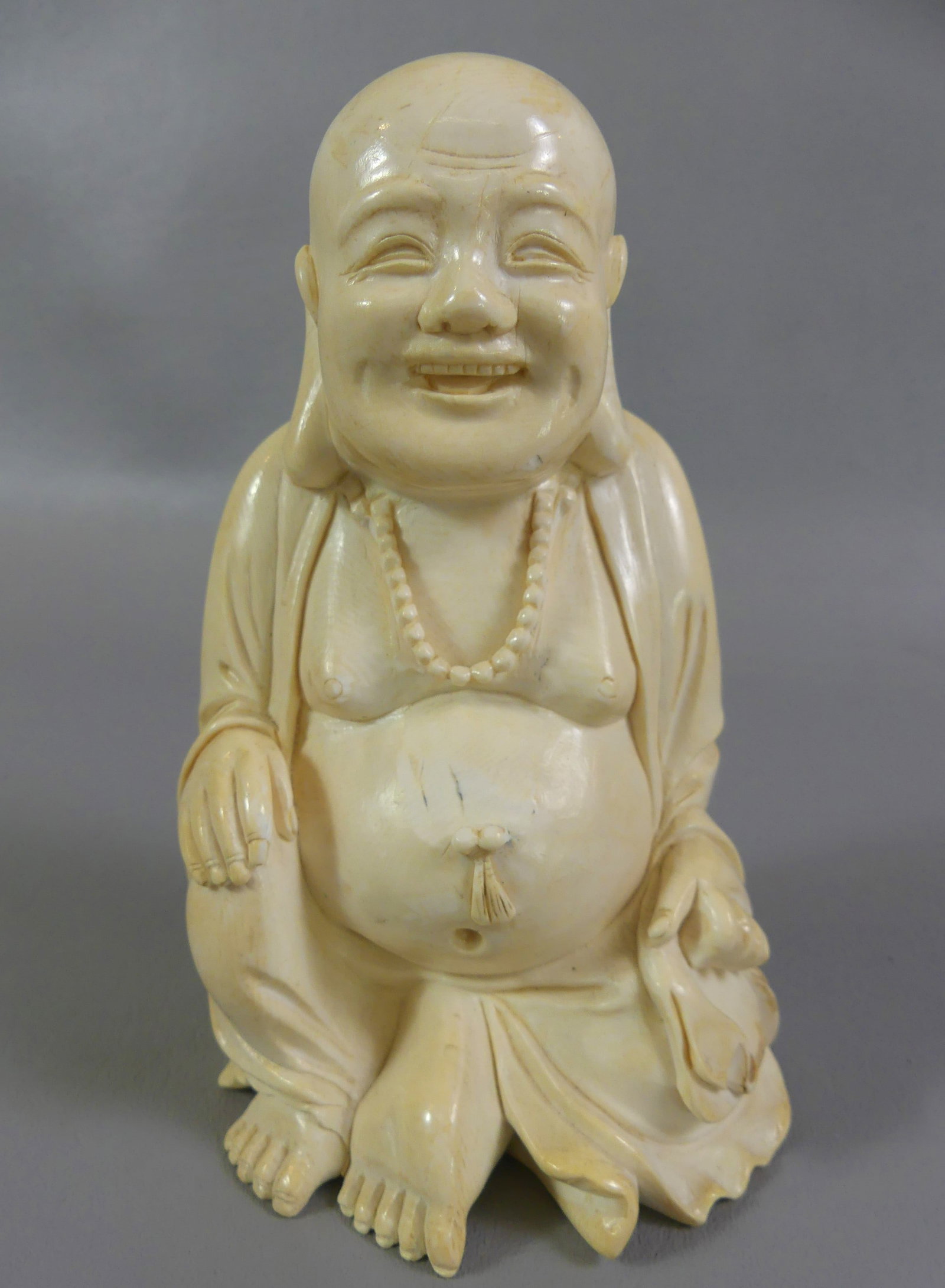 CARVED BONE CHINESE BUDDHA: 19th century solid carved bone Chinese figurine of a smiling, seated buddha. 6 in tall, 3.5 in wide.