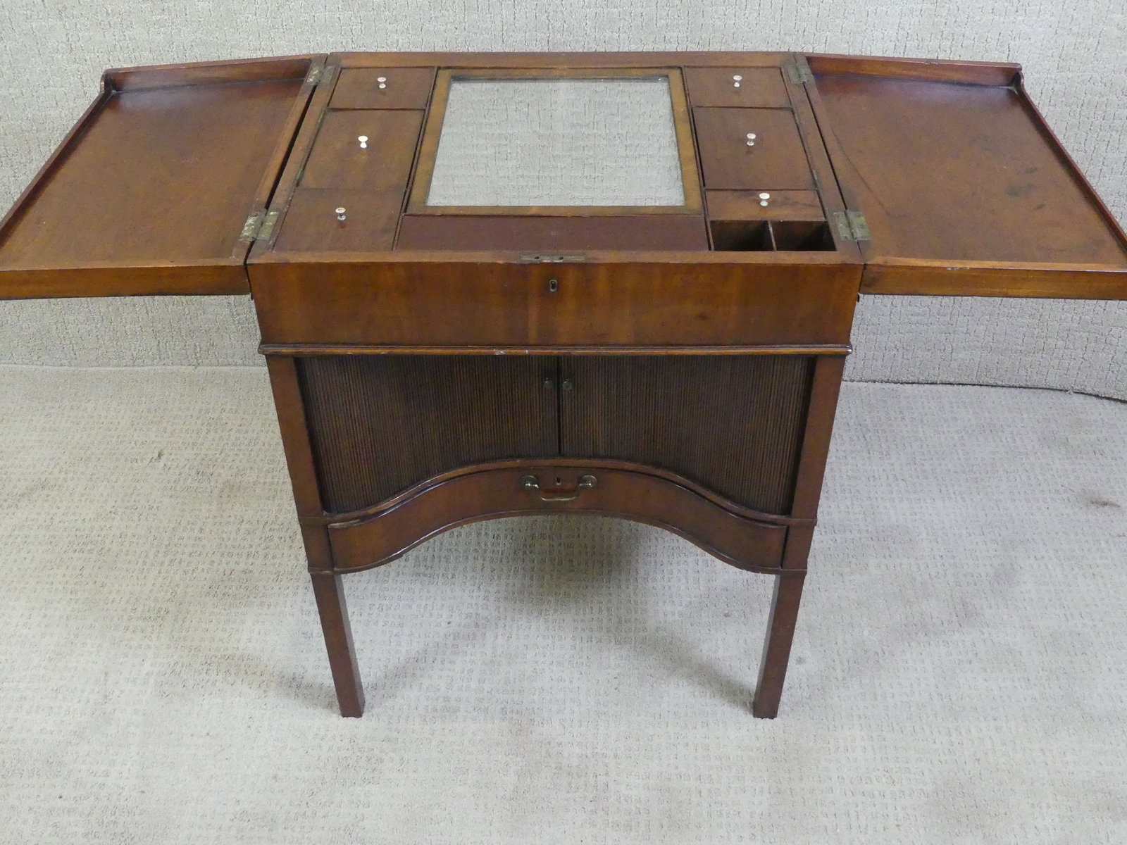 PERIOD ENGLISH TAMBOUR DRESSING TABLE: 19th century English mahogany lift-top vanity table with concave tambour front and single drawer. Interior has several fitted compartments with covers and a mirror. 32 in h x 24 x 20 in closed.