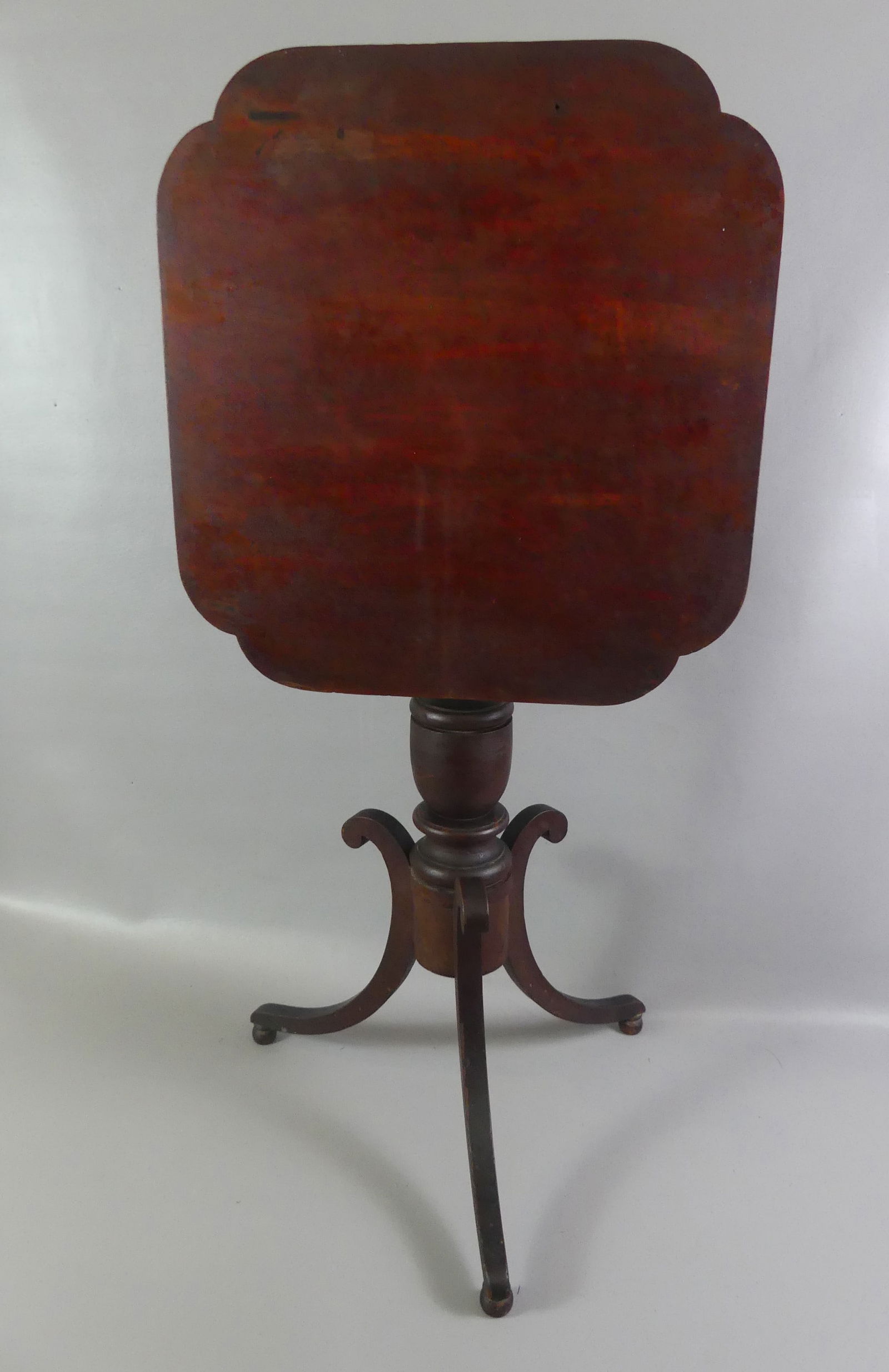 ANTIQUE TILT TOP TABLE: Antique tilt top table with stained reddish surface, tripod legs, turned pedestal and rectangular, shaped top. 29 in high x 21 x 20.