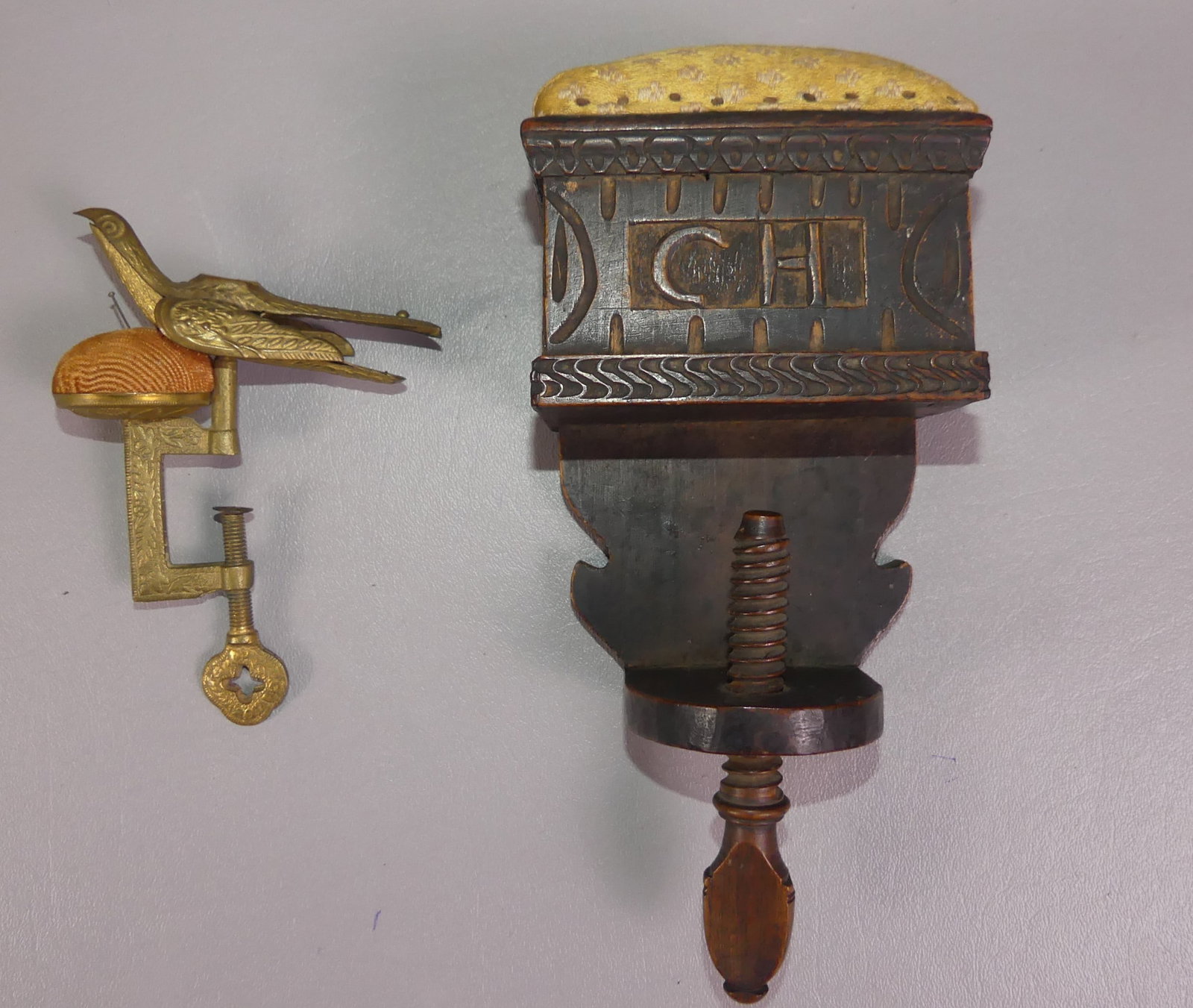2 ANTIQUE SEWING CLAMP PINCUSHIONS: Two 19th century sewing clamps: unusual carved walnut with side drawer and initials CH, 8 x 4 x 2.5 in; and a fancy brass sewing bird with pin cushion top.