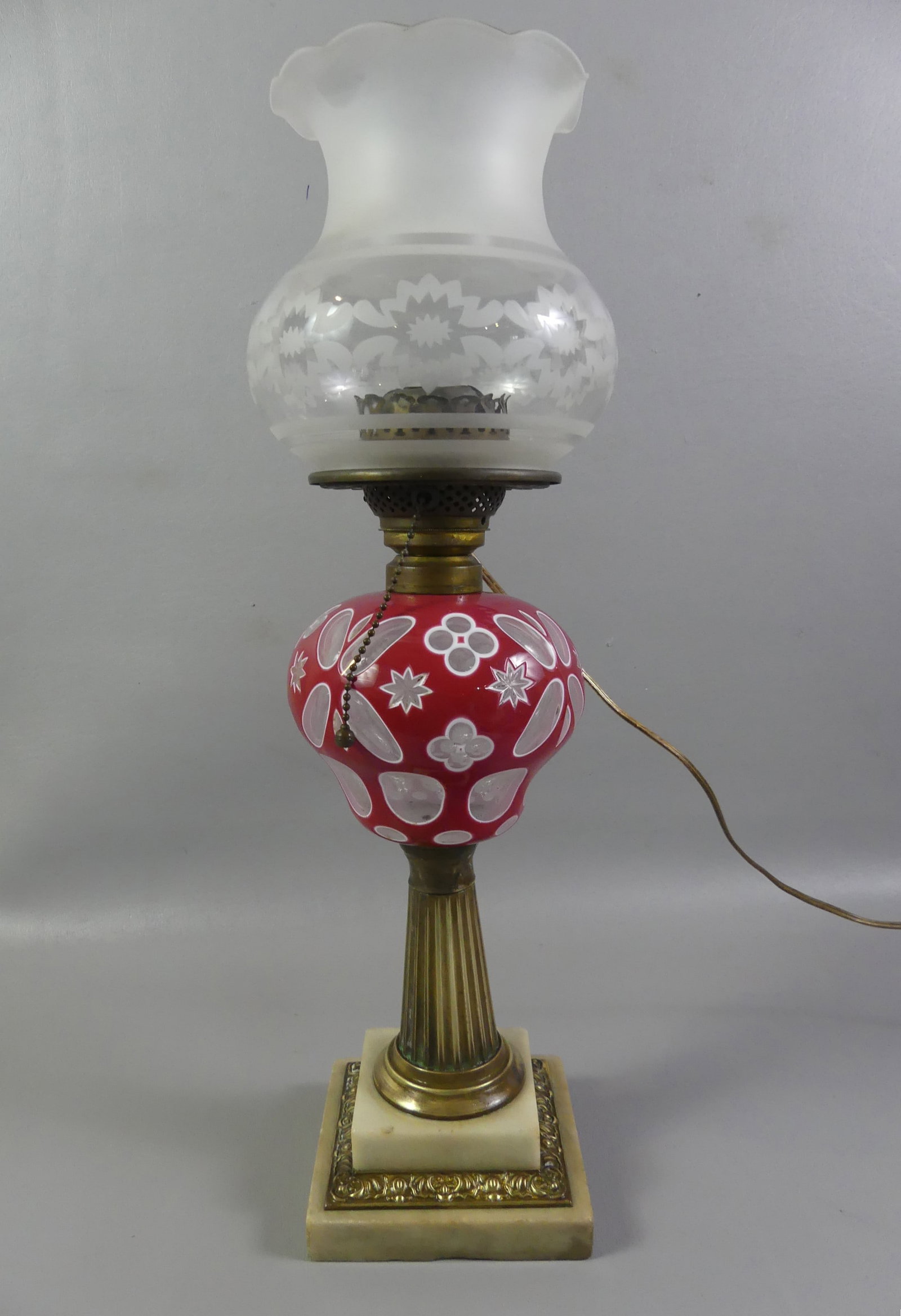 SANDWICH GLASS OVERLAY OIL LAMP - RED: Sandwich Glass double overlay oil lamp in red and white with geometric designs, brass column and marble base. It has a cut and frosted glass shade with 4 inch fitter. Has been properly electrified fro
