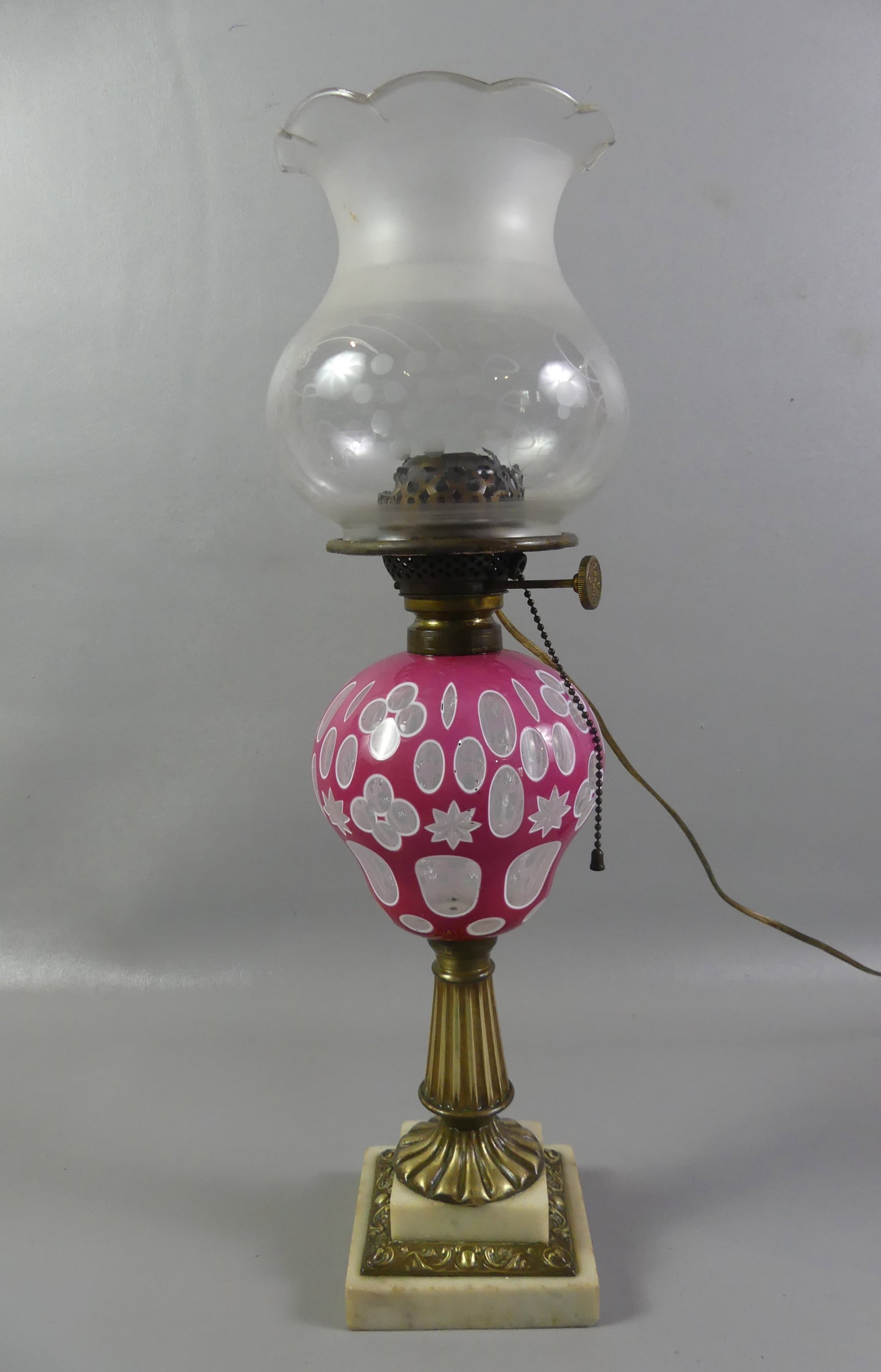 SANDWICH GLASS OVERLAY OIL LAMP - PINK: Sandwich Glass double overlay oil lamp in pink and white with geometric designs, brass column and marble base. It has a cut and frosted glass shade with grape motif. Has been properly electrified from