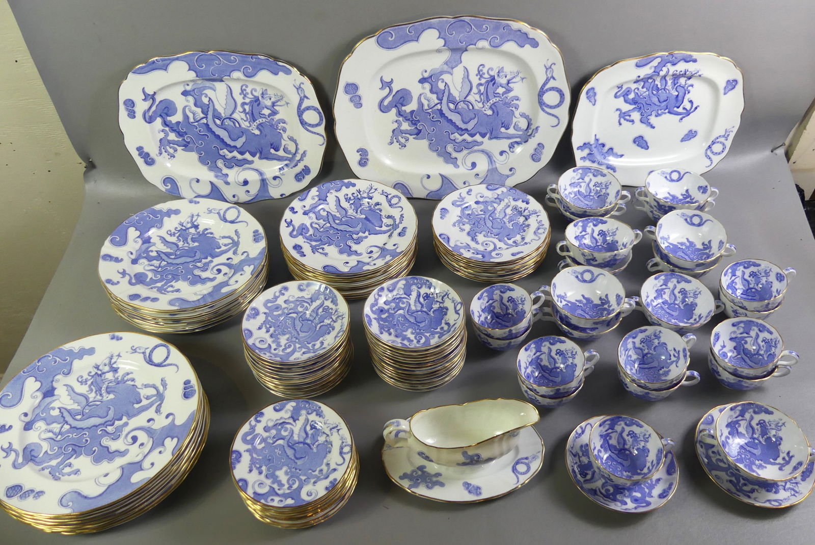 ROYAL WORCESTER BLUE DRAGON DINNER SET: Striking Royal Worcester Blue Dragon pattern porcelain dinner set with gold rims consisting of: 3 platters to 16.5 in long; 9 dinner plates 10.5 in; 8 ribbed dinner plates 10.5 in; 11 luncheon plates,